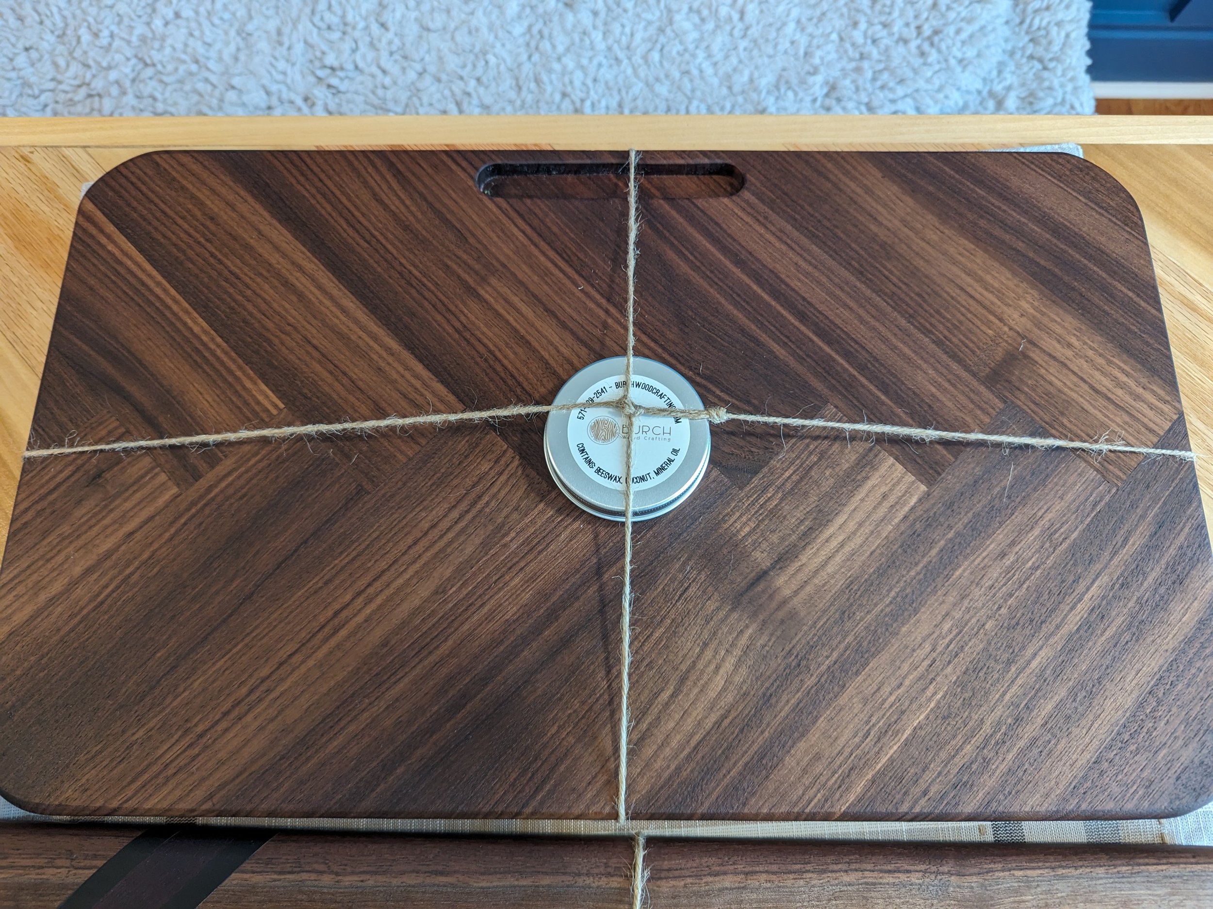 Wooden cutting board with a round wax container in the center and twine crossing over it.