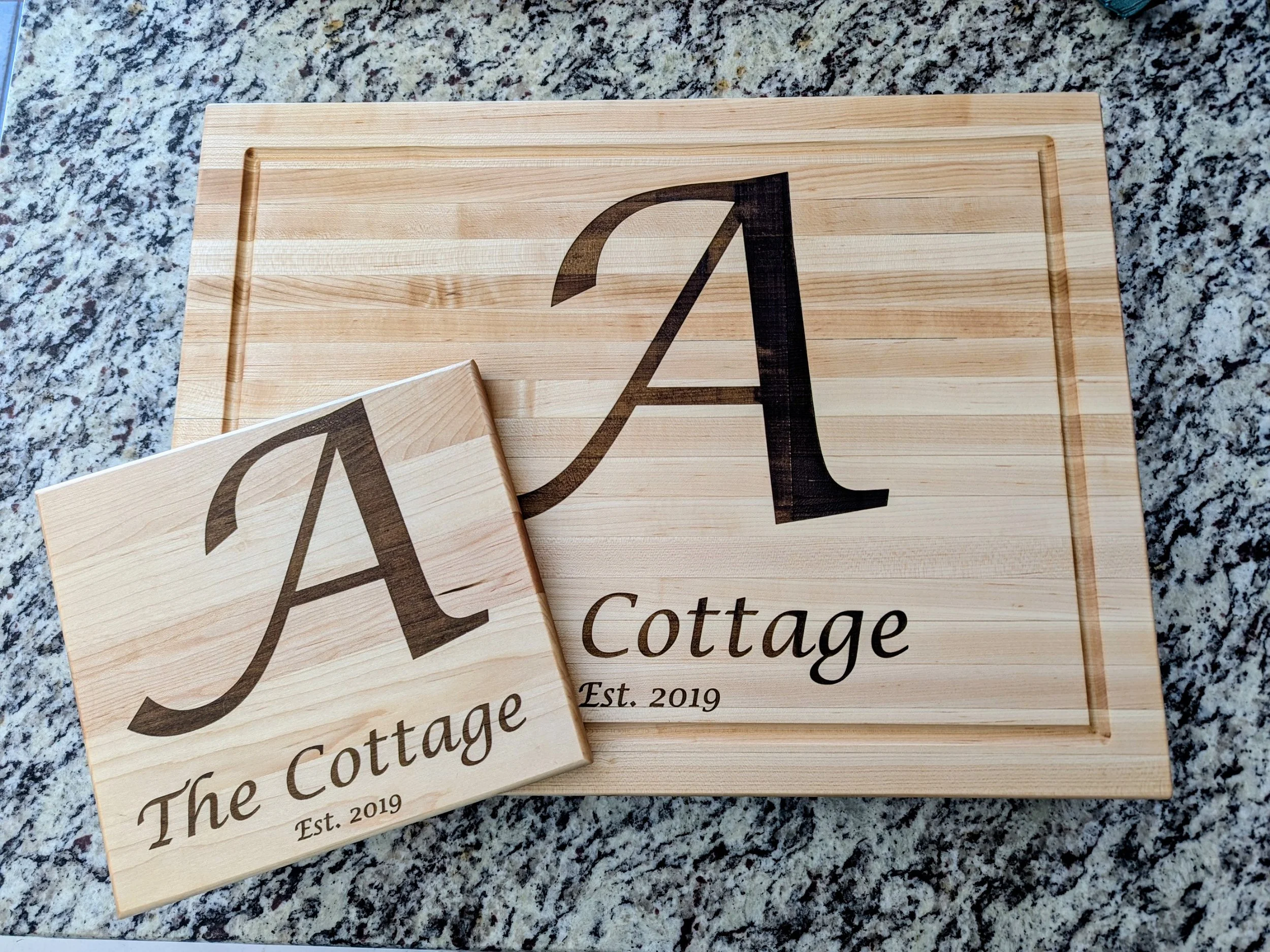 Matching small and large cutting boards laser engraved with the letter 'A' representing the family name, 'Est. 2019' and 'The Cottage.'