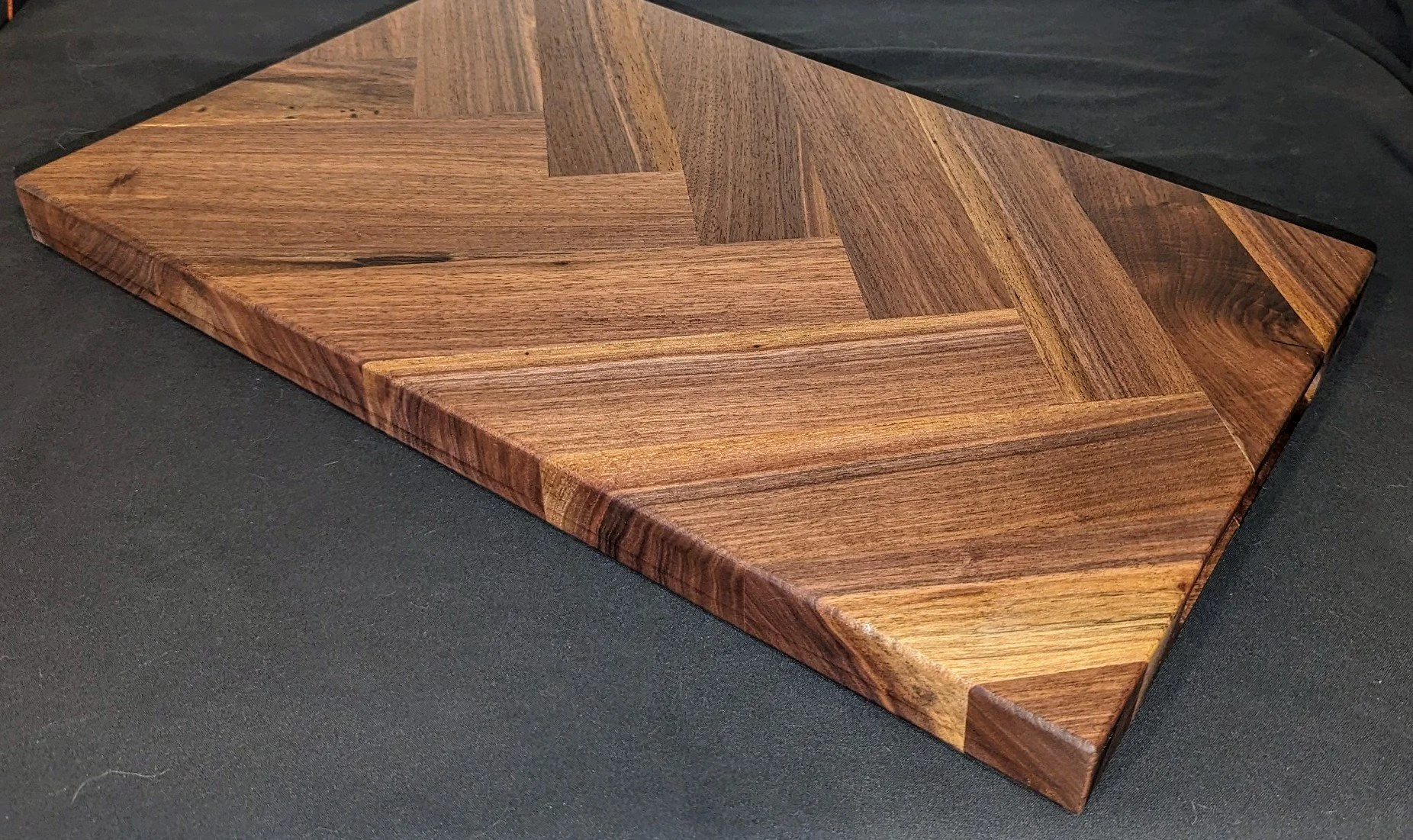 Close-up of a wooden cutting board with a chevron pattern, resting on a black surface.