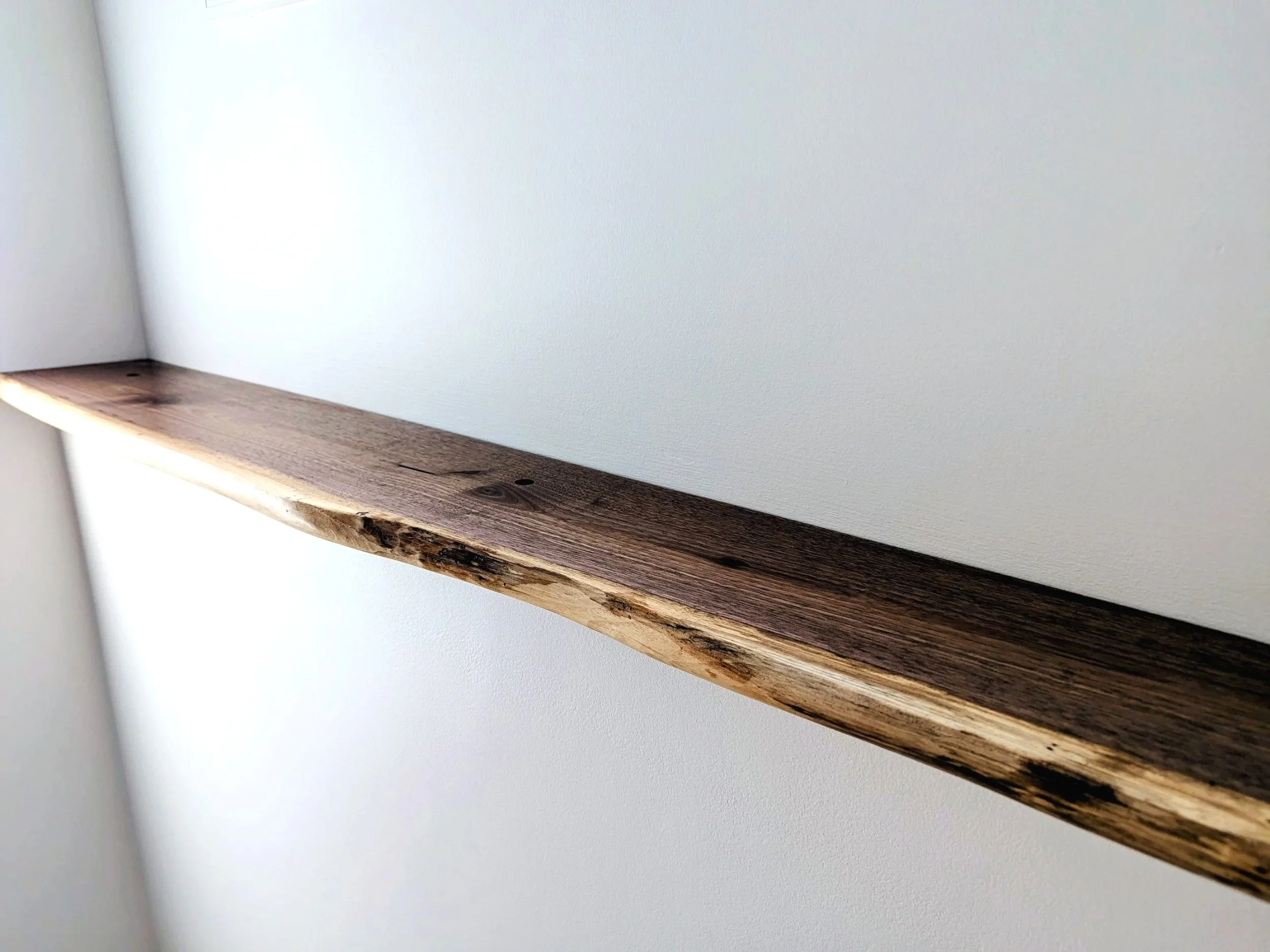 Close-up of a wooden shelf mounted on a white wall, showing natural wood grain and some imperfections.
