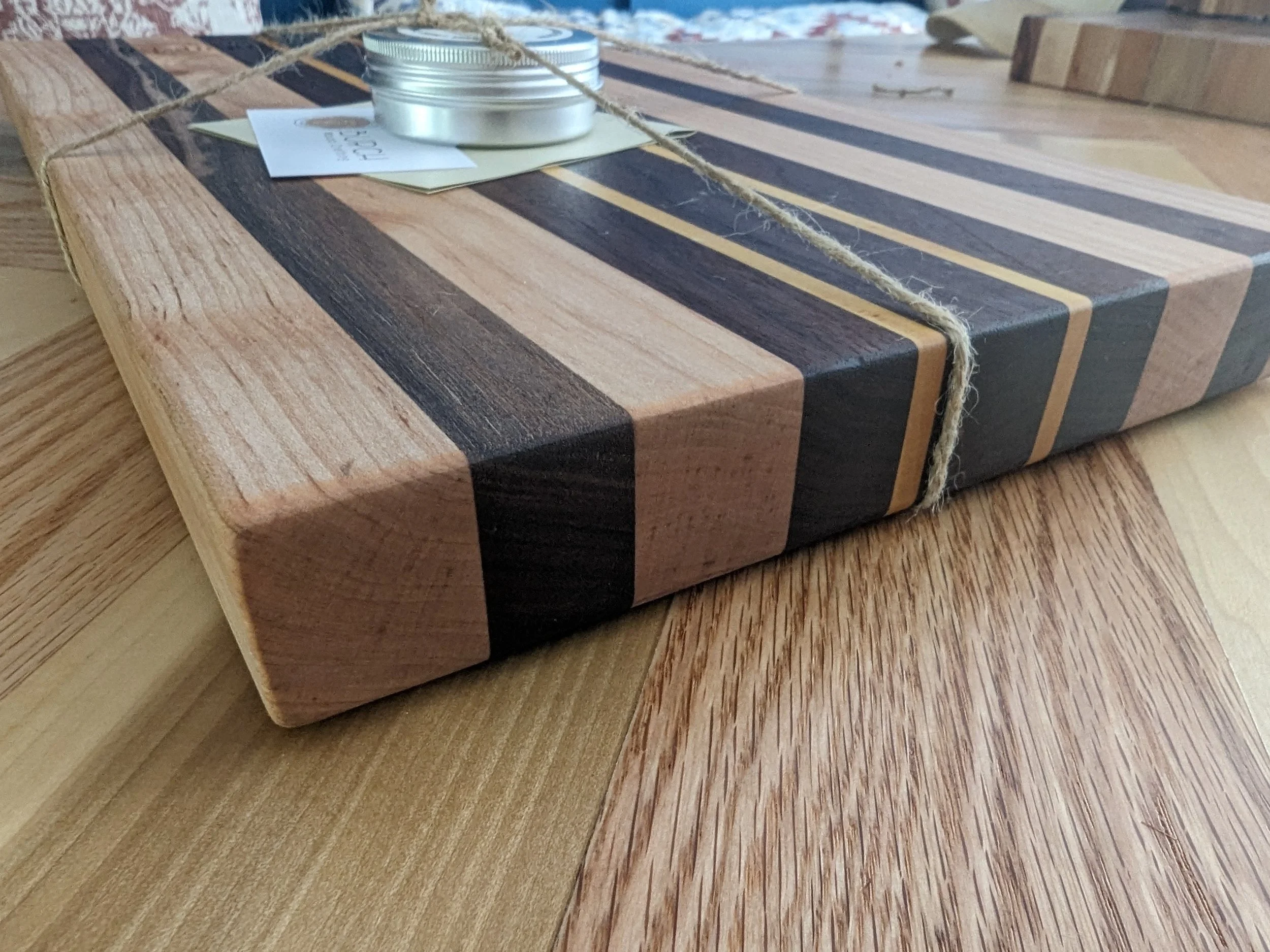 A wooden board with a striped pattern of dark and light wood, tied with a string and labeled, placed on a wooden surface.