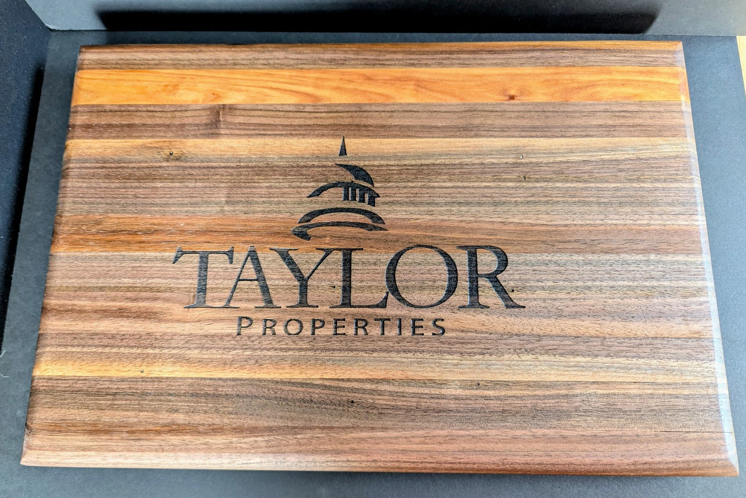 Wooden sign with black engraved text reading "Taylor Properties" and a lighthouse logo above the text.