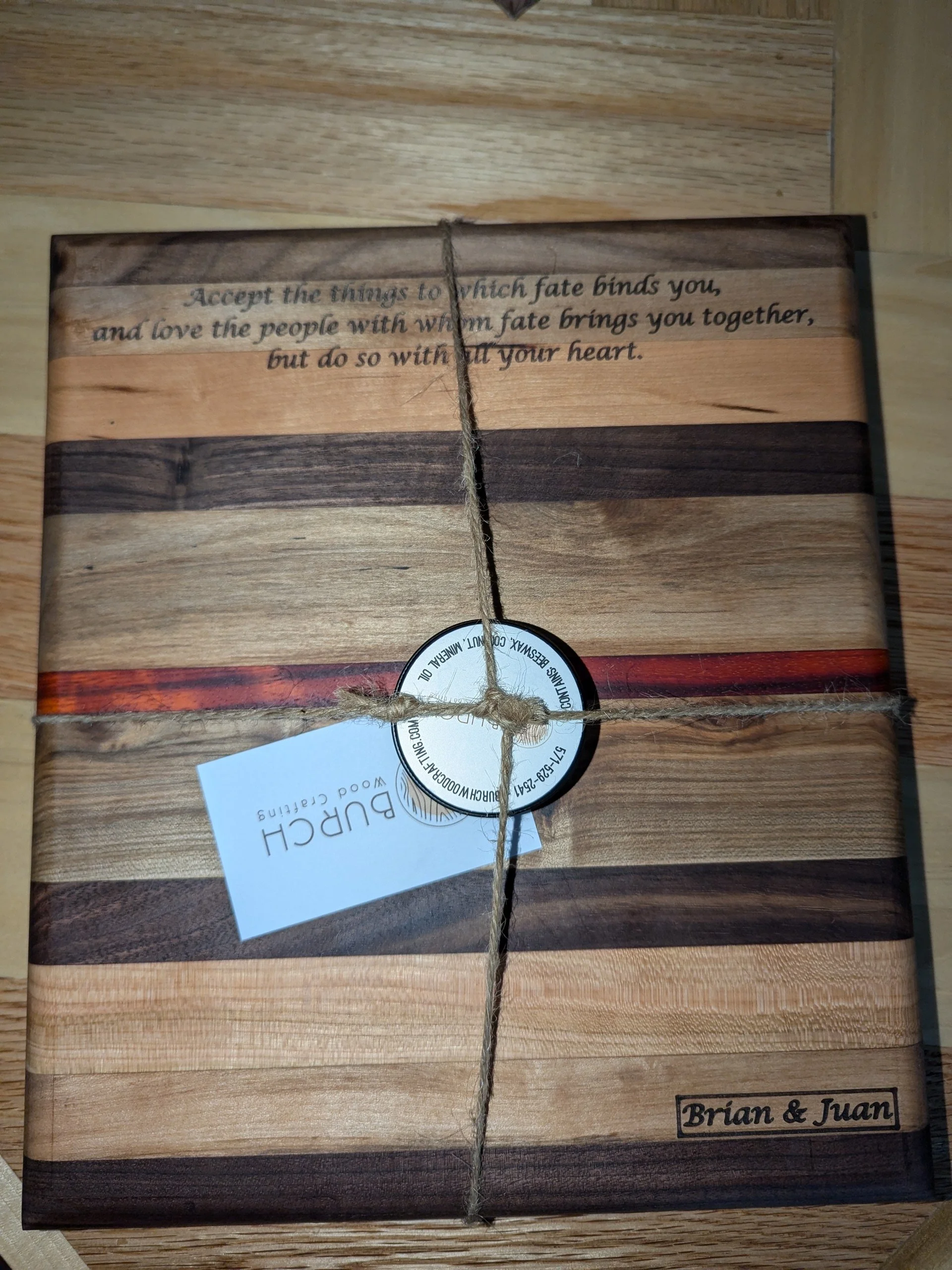 A wooden cutting board with a quote engraved on it, secured with twine and a circular tag. The quote reads, "Accept the things to which fate binds you, and love the people with whom fate brings you together, but do so with all your heart." The board 