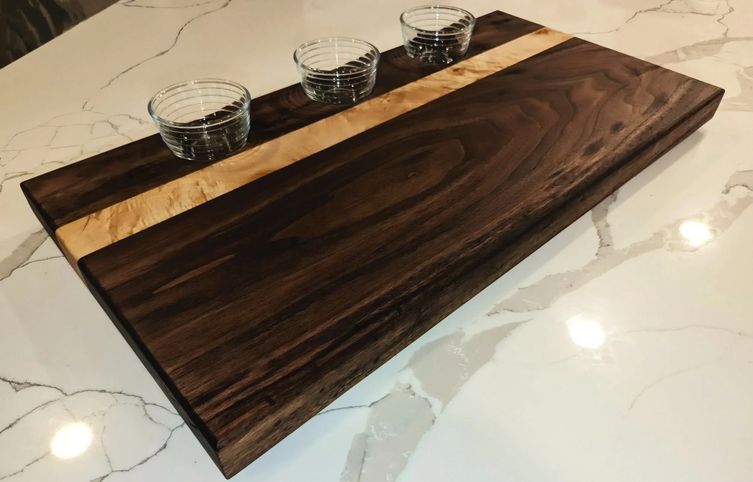 A wooden serving platter with three glass bowls on a white marble countertop.