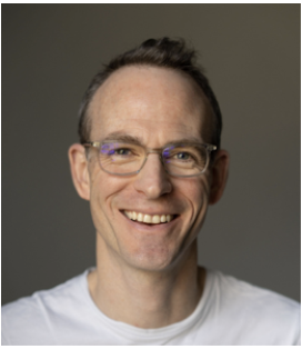 Close-up of a smiling man with glasses and short brown hair, wearing a white shirt