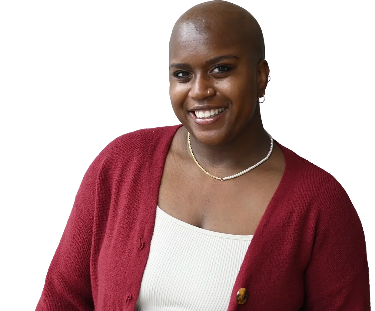 A woman with a shaved head, smiling, wearing a red cardigan, white top, pearl necklace, and earrings.