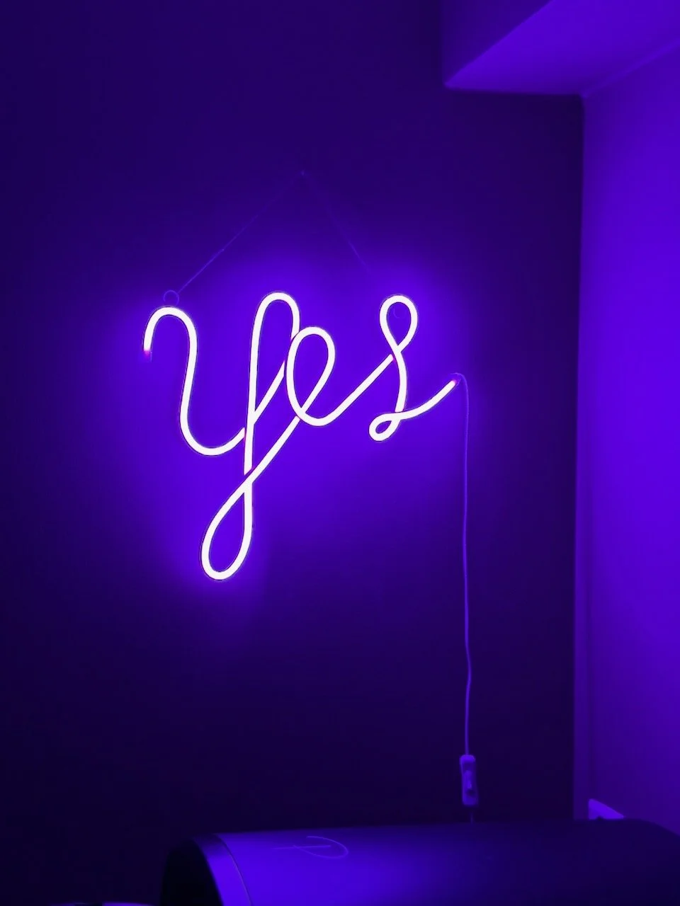 Interiørdesign av Angela Schrøder. Neonskilt med ordet 'yes' i lilla lys, hengende på en mørk vegg.