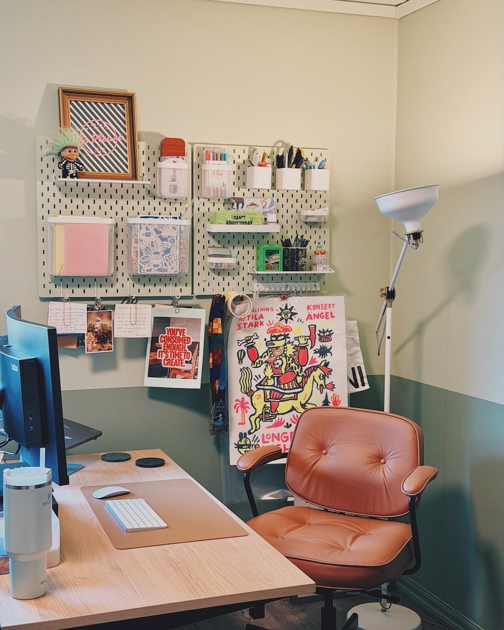 Interiørdesign av Angela Schrøder. Et hjemmekontor med et skrivebord med dataskjerm og tastatur, en komfortabel lenestol, et gulvlampa og en vegg med oppbevaringsløsninger og dekorasjoner.
