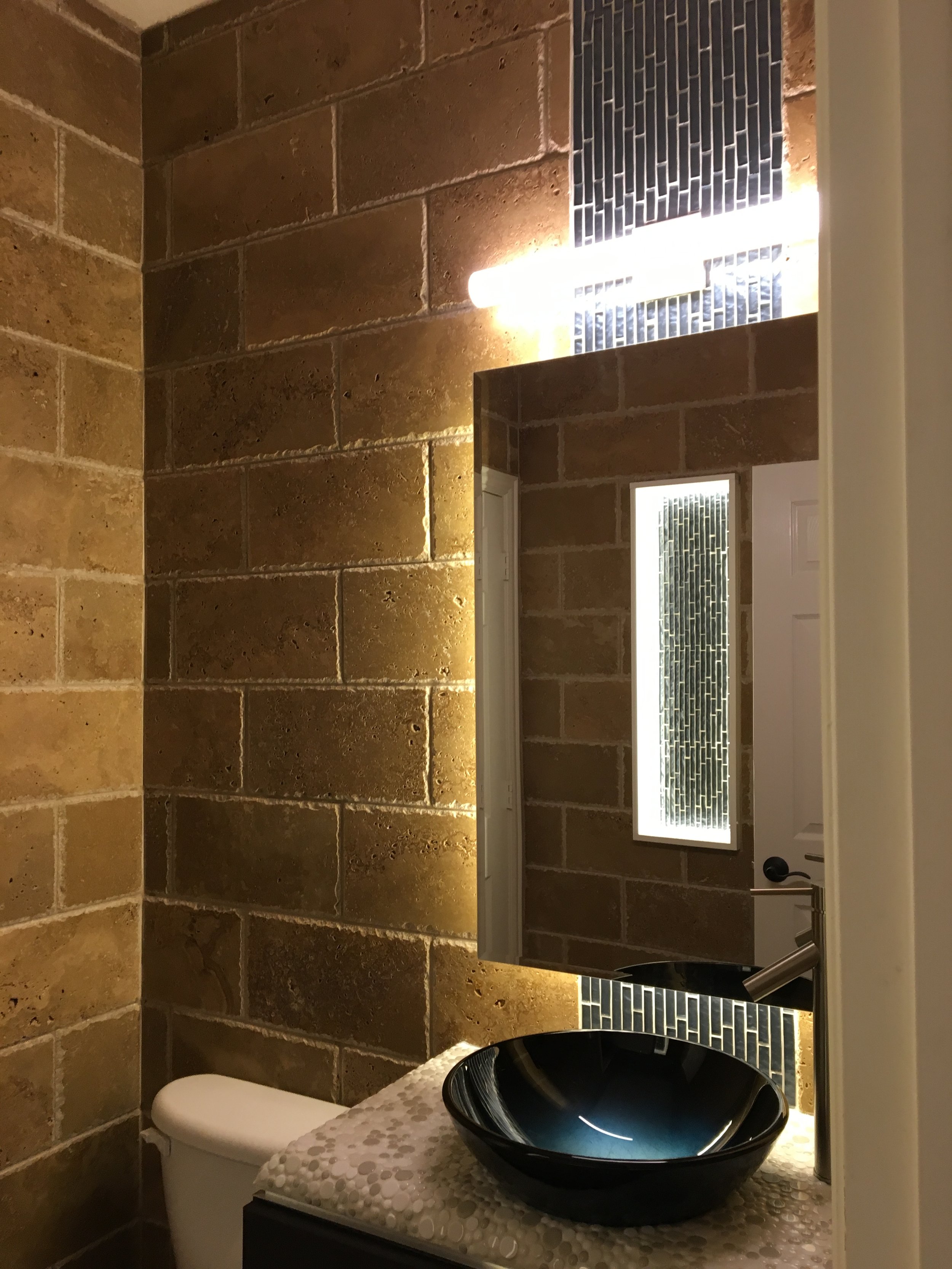 Half Bathroom: Close-up of custom waterfall tiling with a floating mirror and bubble-texture stone countertop