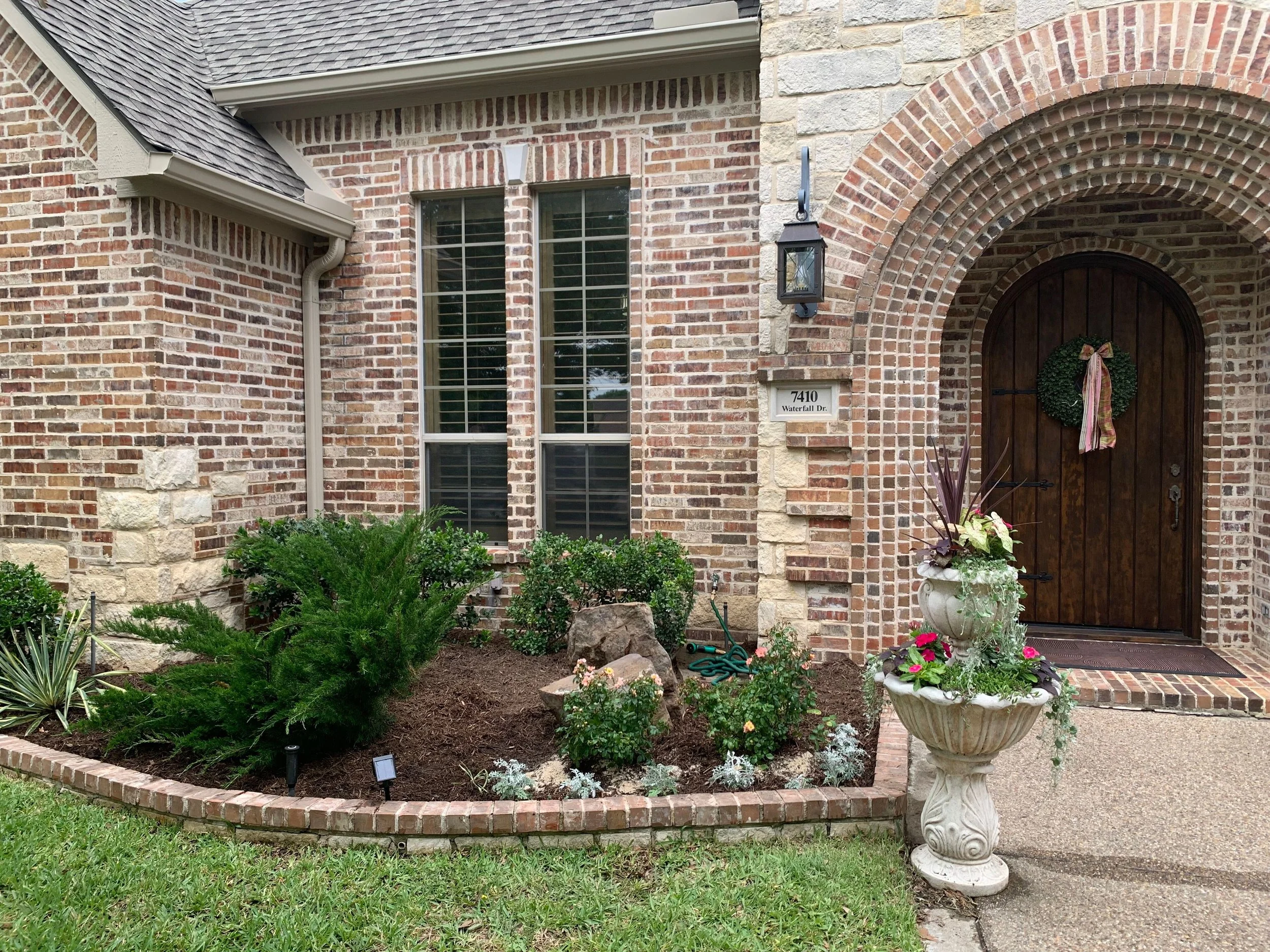 Landscape: Leyland cypress relocated from the backyard, dusty millers transplanted from existing pots, and new Peach Drift Roses installed. Two new moss boulders add a stunning focal point to complete this front yard transformation.