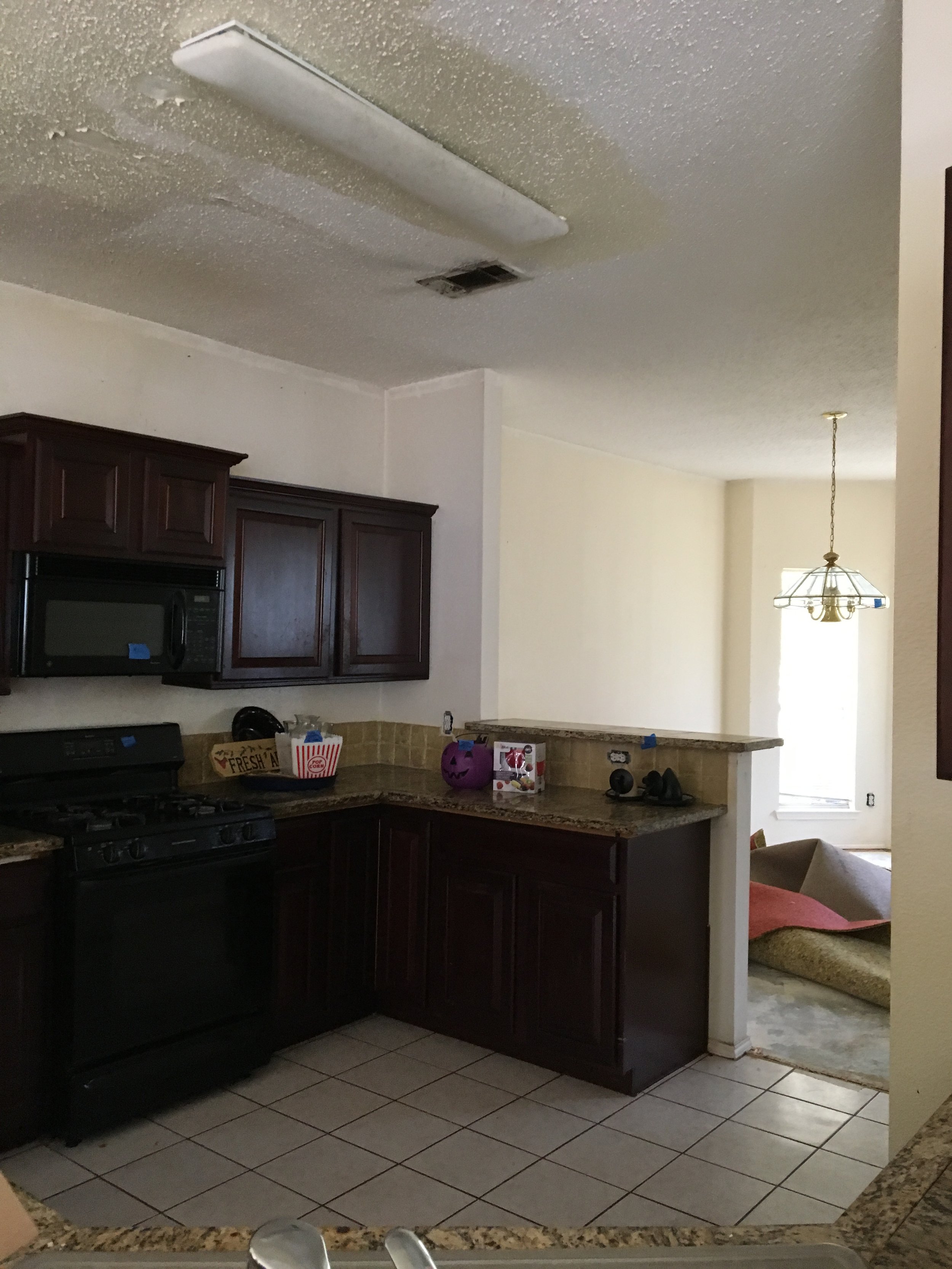 Kitchen: Original dark cabinetry and heavy finishes created a stark contrast with the sunlit adjacent dining room, making the kitchen feel isolated and dim (Before)