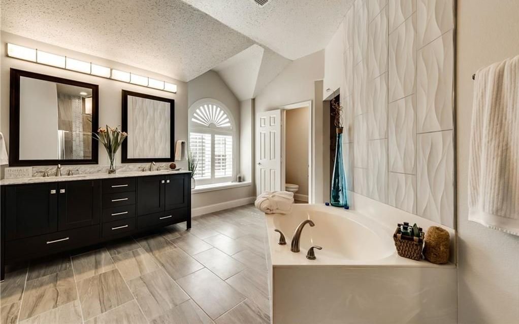 Primary Bathroom: Full renovation featuring new vanities, mirrors, lighting, an interior door, cohesive color tones, and updated floor and wall tiling