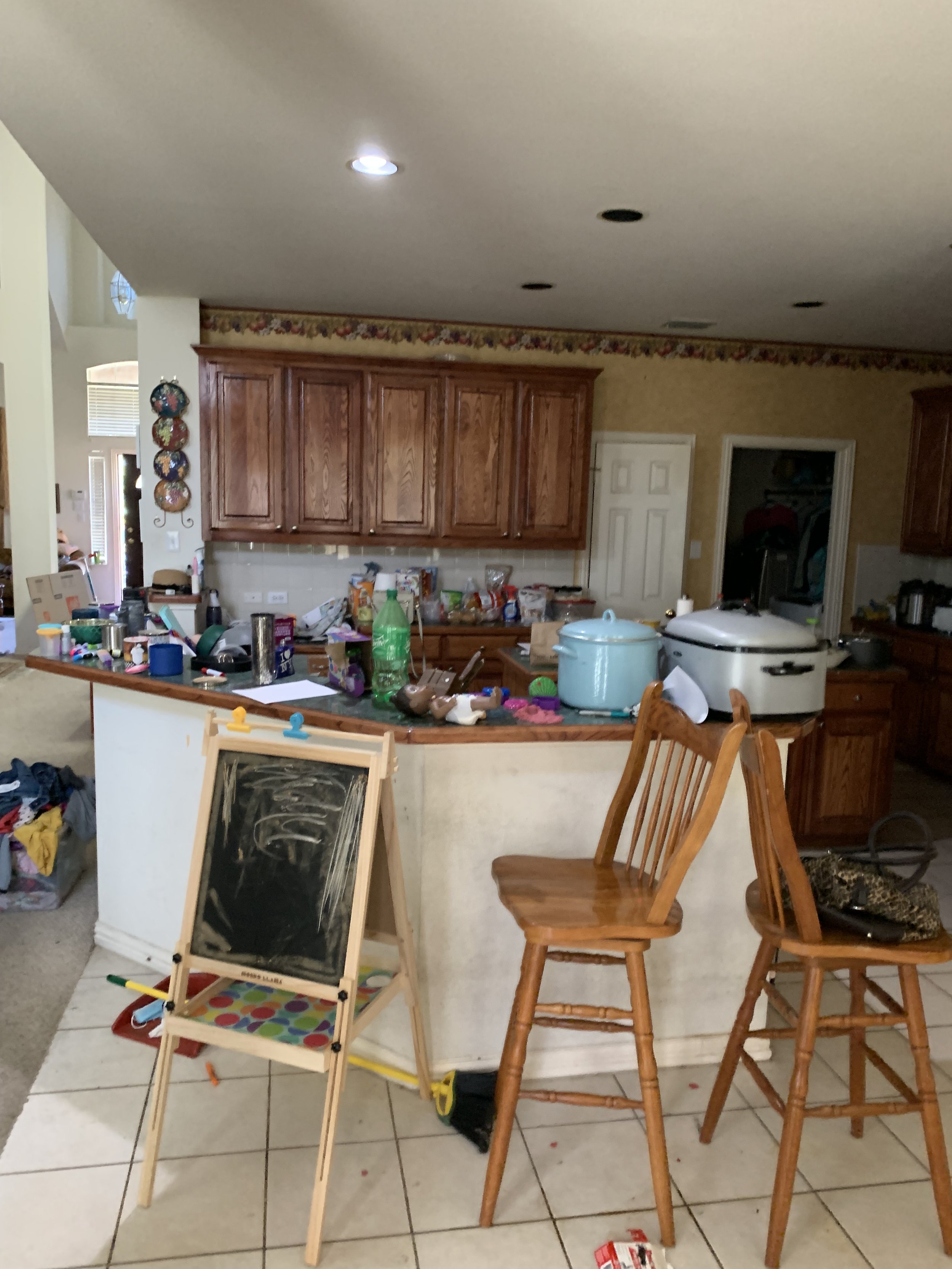 Kitchen: Original combination of dark cabinetry, lighting, countertops, and dated wallpaper created a heavy, dark environment (Before)