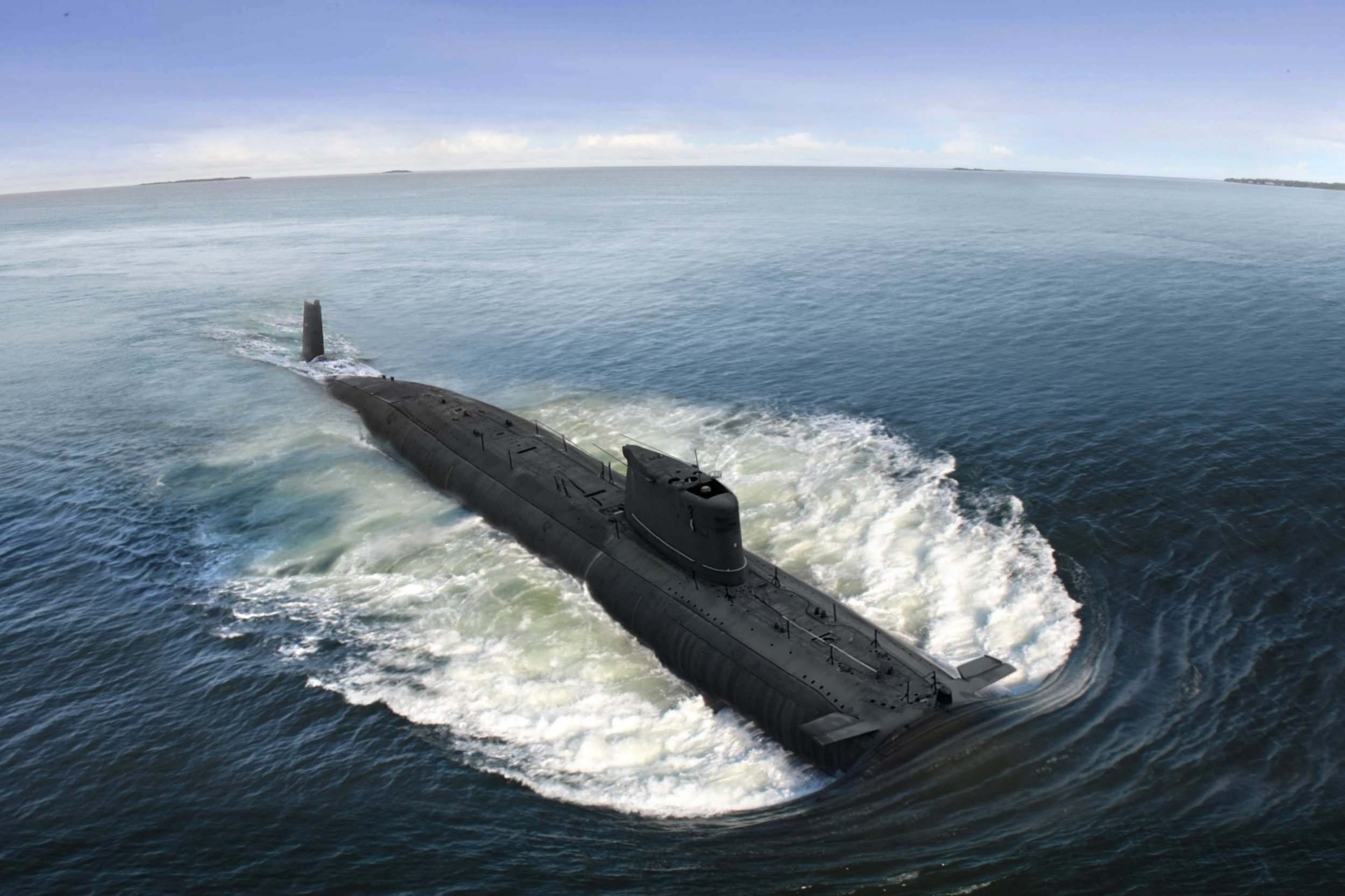 A submarine moving through open ocean water with distant islands on the horizon under a partly cloudy sky.