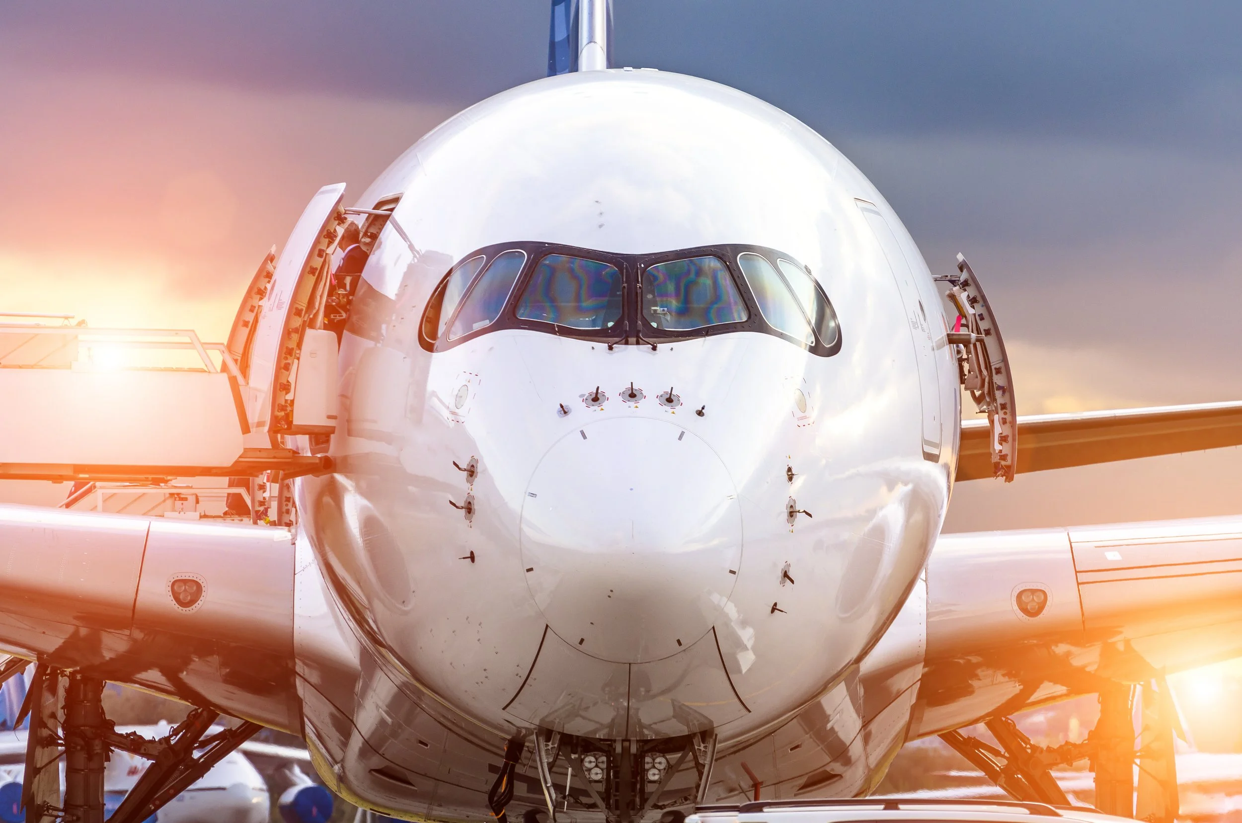 A close-up of the nose of a white spacecraft or space shuttle on a launch pad with open hatches and scaffolding, against a partly cloudy sky at sunset.