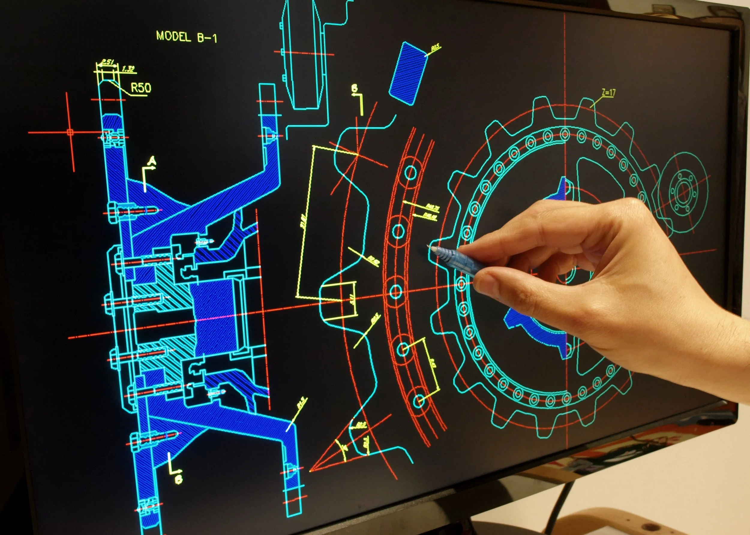A person holding a stylus writes on a large digital screen displaying a technical engineering blueprint with detailed diagrams, measurements, and annotations.