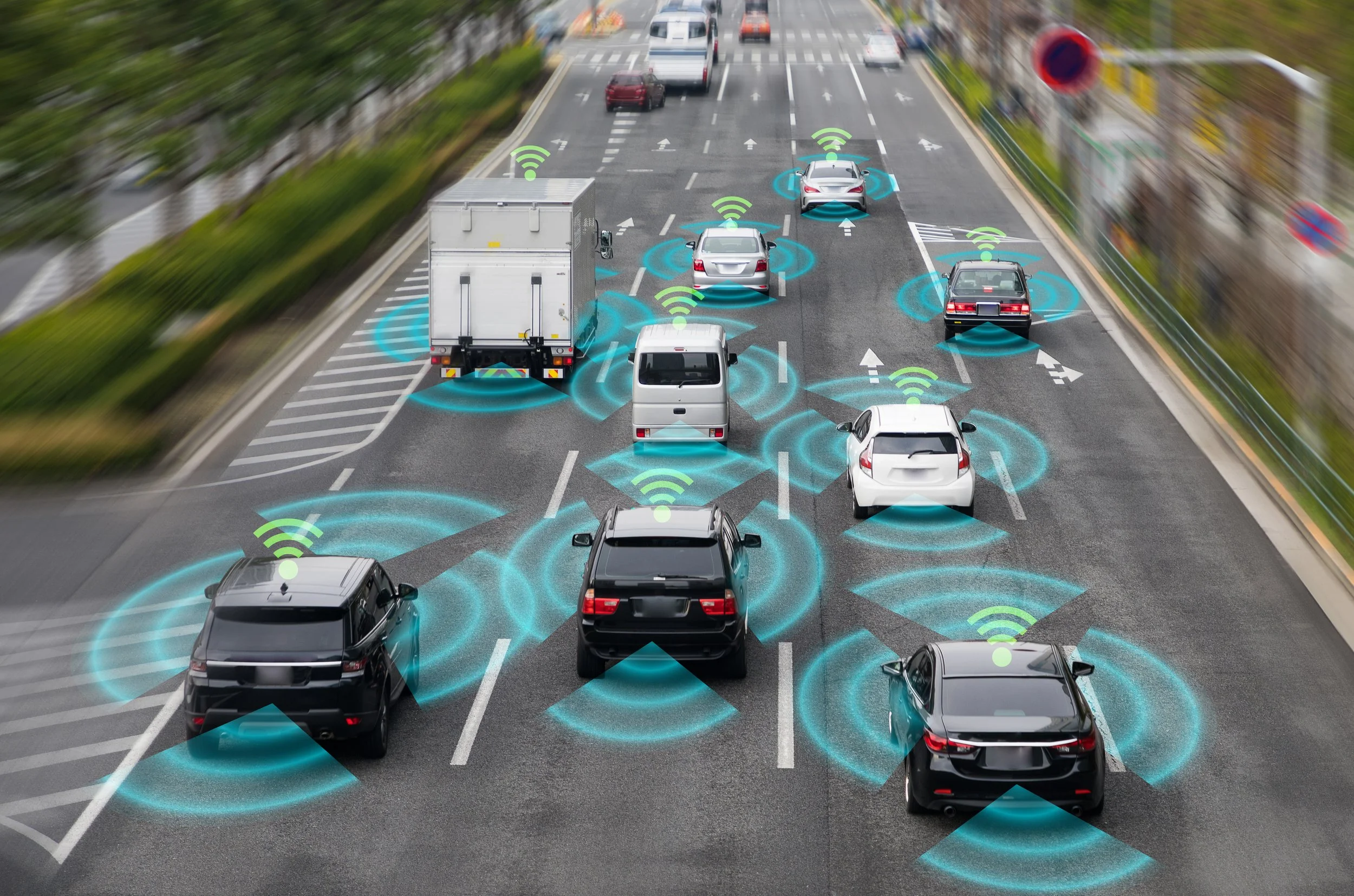 Multiple cars on a busy multi-lane highway with digital overlays indicating wireless communication signals between vehicles, representing connected autonomous cars.