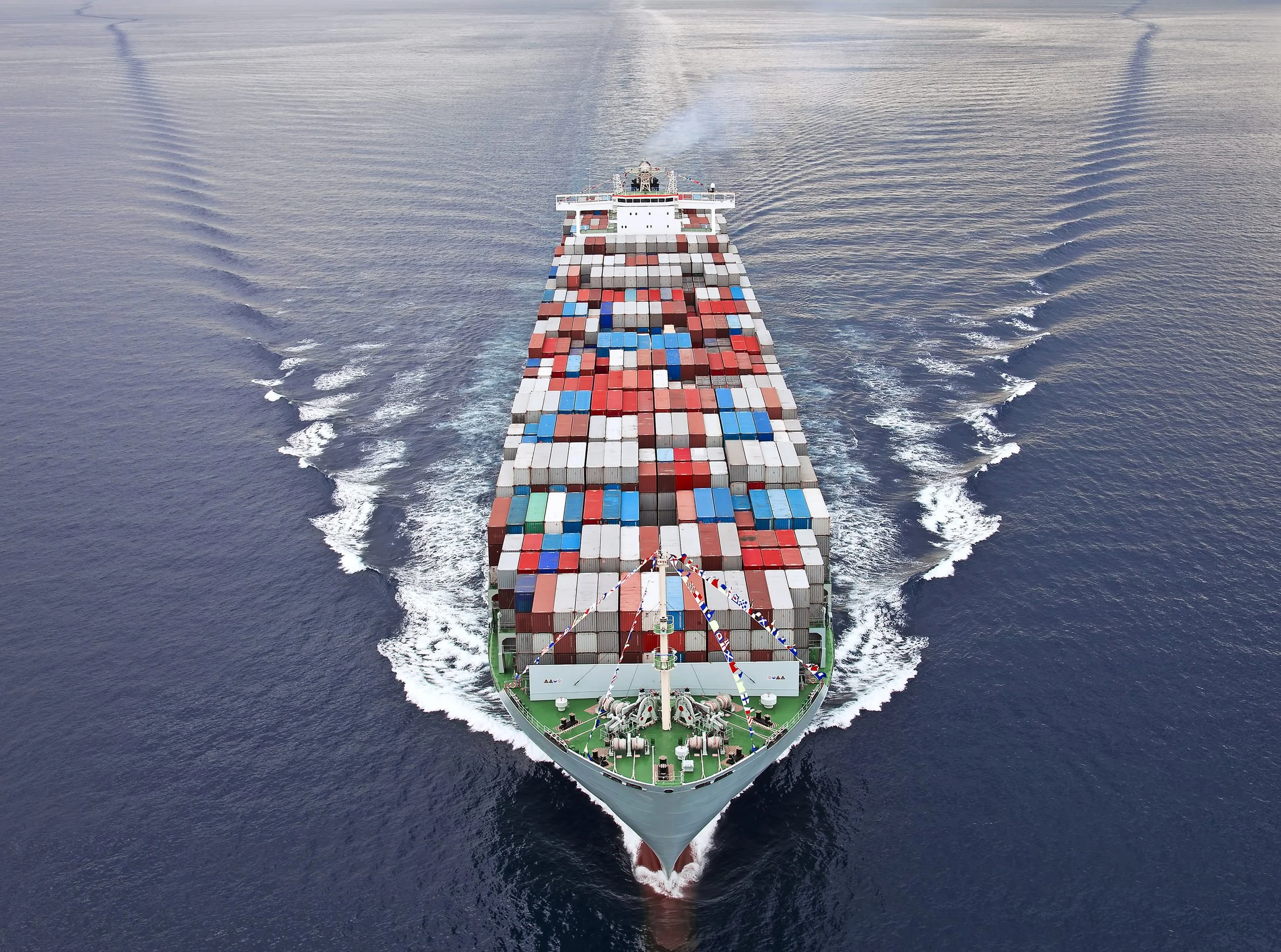 A cargo ship sailing on the ocean carrying numerous colorful shipping containers.