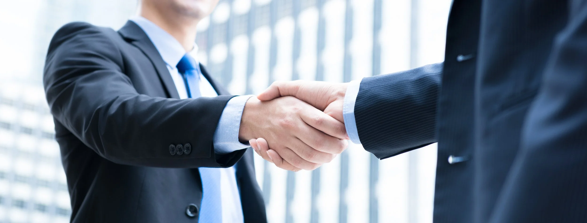 Two business professionals shaking hands in a modern office building.
