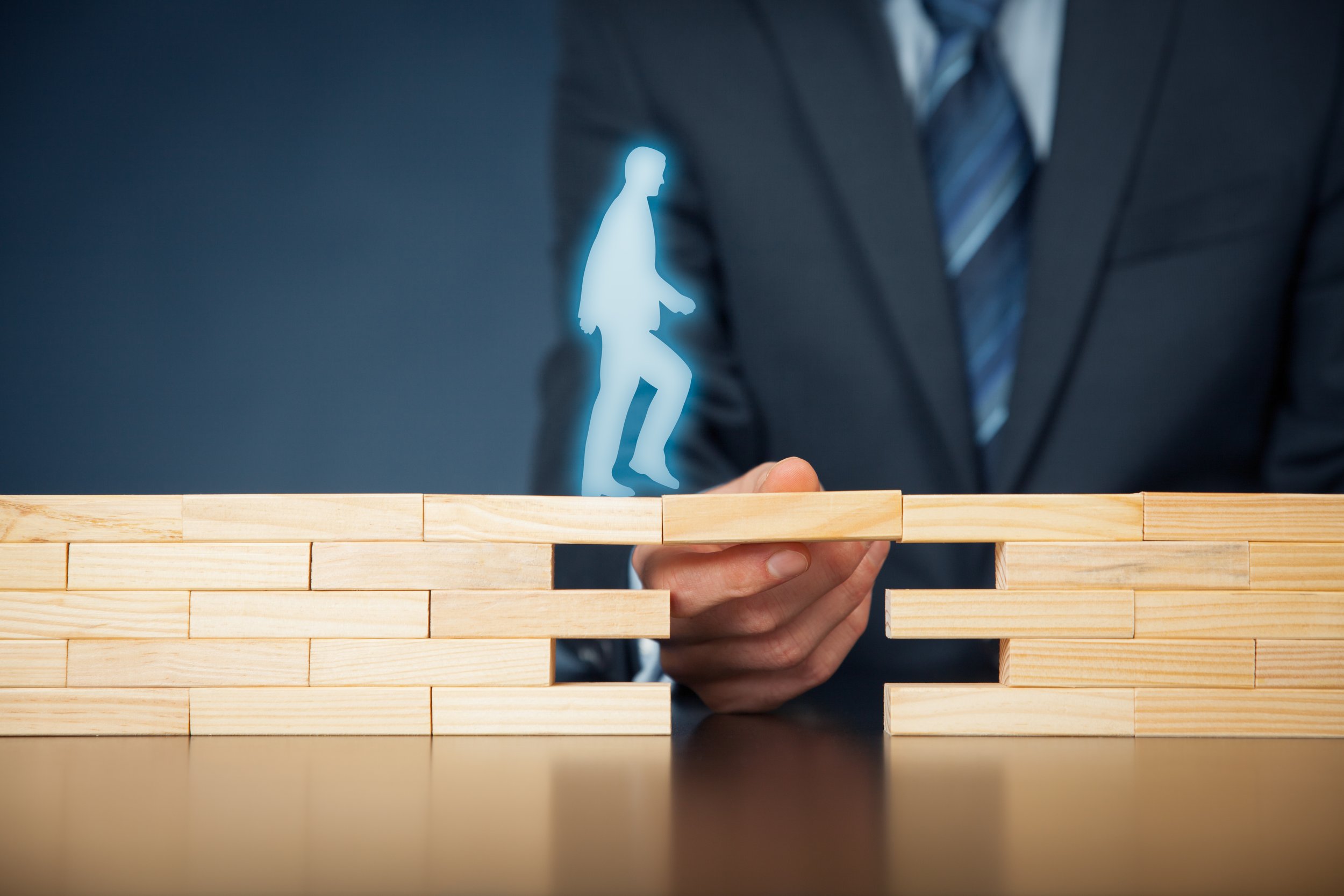 Person in business suit with striped tie holding a wooden block with a glowing holographic silhouette of a walking person above it.