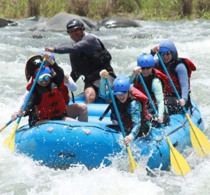 Group of people whitewater rafting on a river, wearing helmets and life jackets, paddling together and smiling.