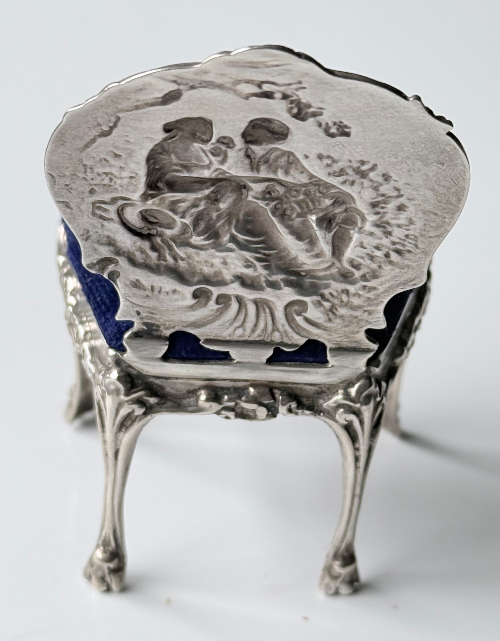 Silver ring with an engraved scene of two children playing, supported by three-legged stands.