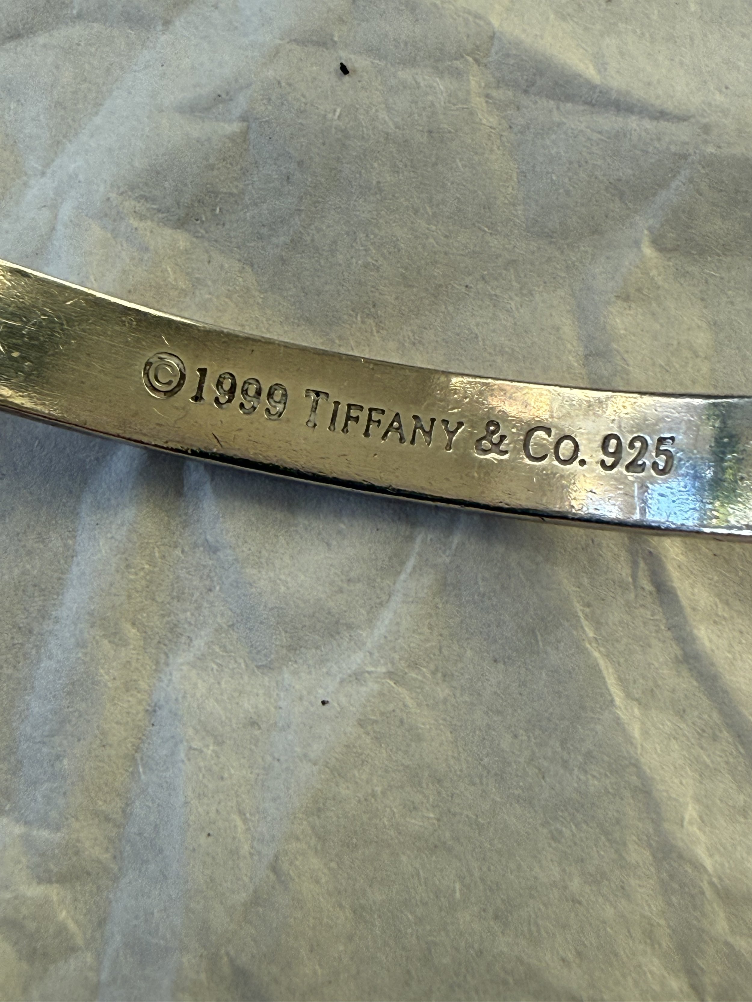 Close-up of a piece of jewelry showing a Tiffany & Co. hallmark engraved with the year 1999, copyright symbol, and '.925' indicating sterling silver.