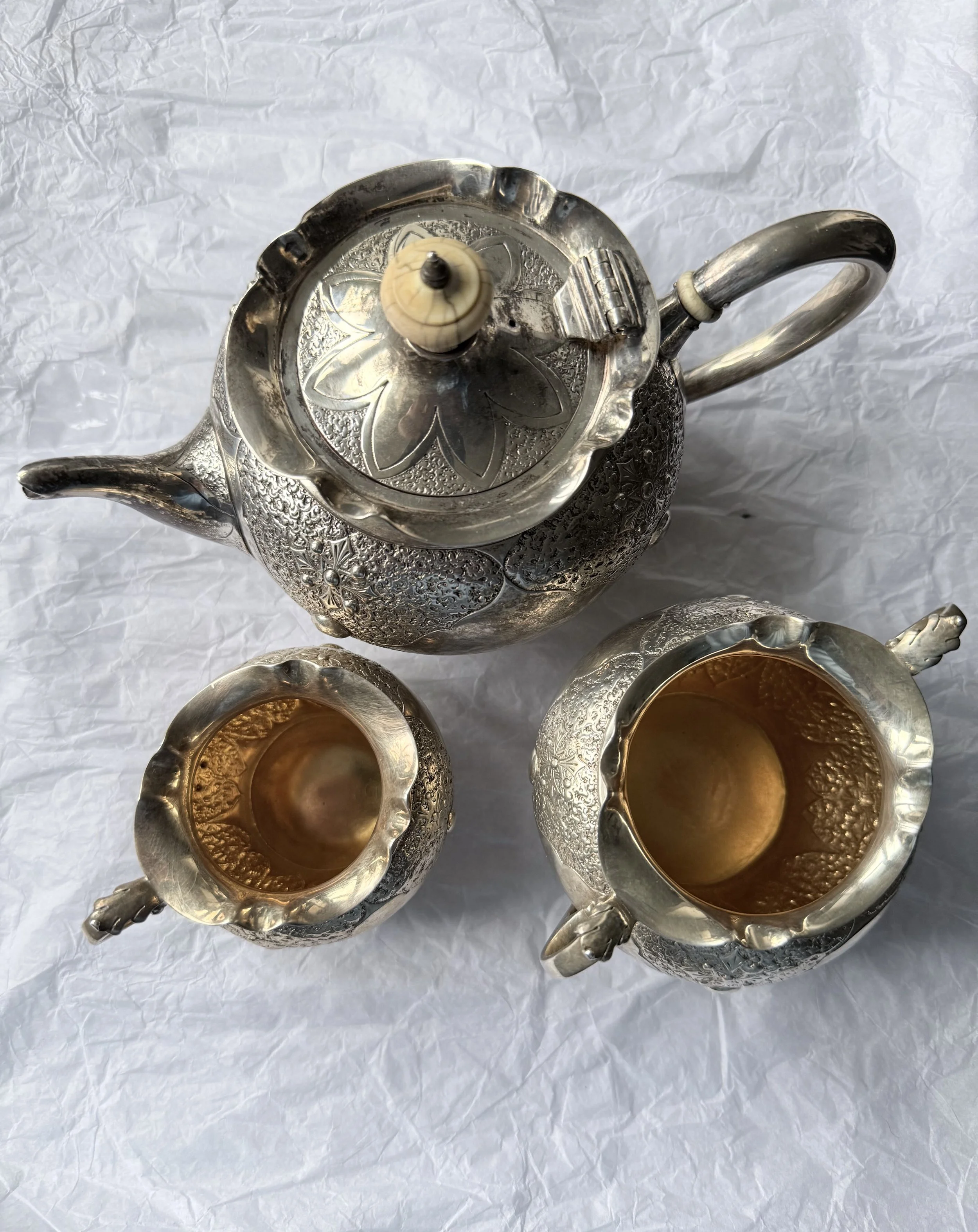 Decorative silver tea set including a teapot with cream and sugar.