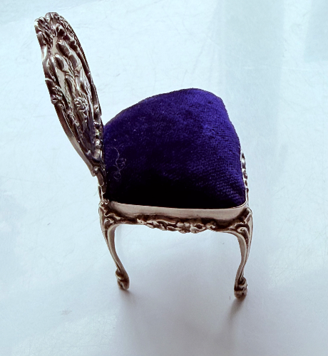 A vintage ornate silver chair with a dark blue pin cushion.