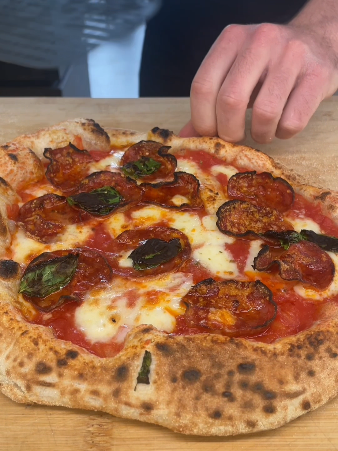A freshly baked pizza with pepperoni, basil leaves, melted cheese, tomato sauce, and a crispy crust, placed on a wooden board.
