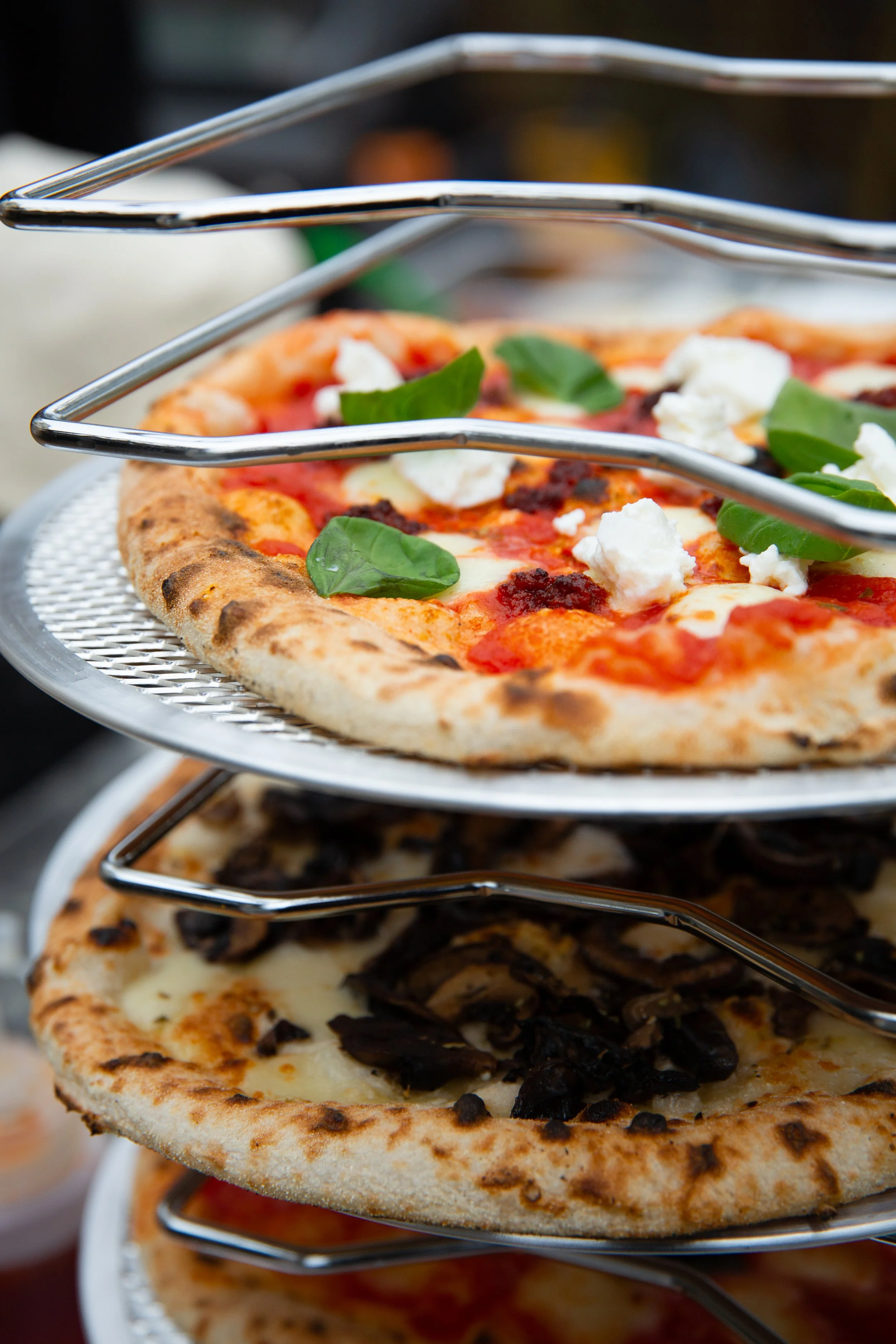 Multiple pizzas on a tiered metal serving stand, with toppings including basil, cheese, tomatoes, and mushrooms.