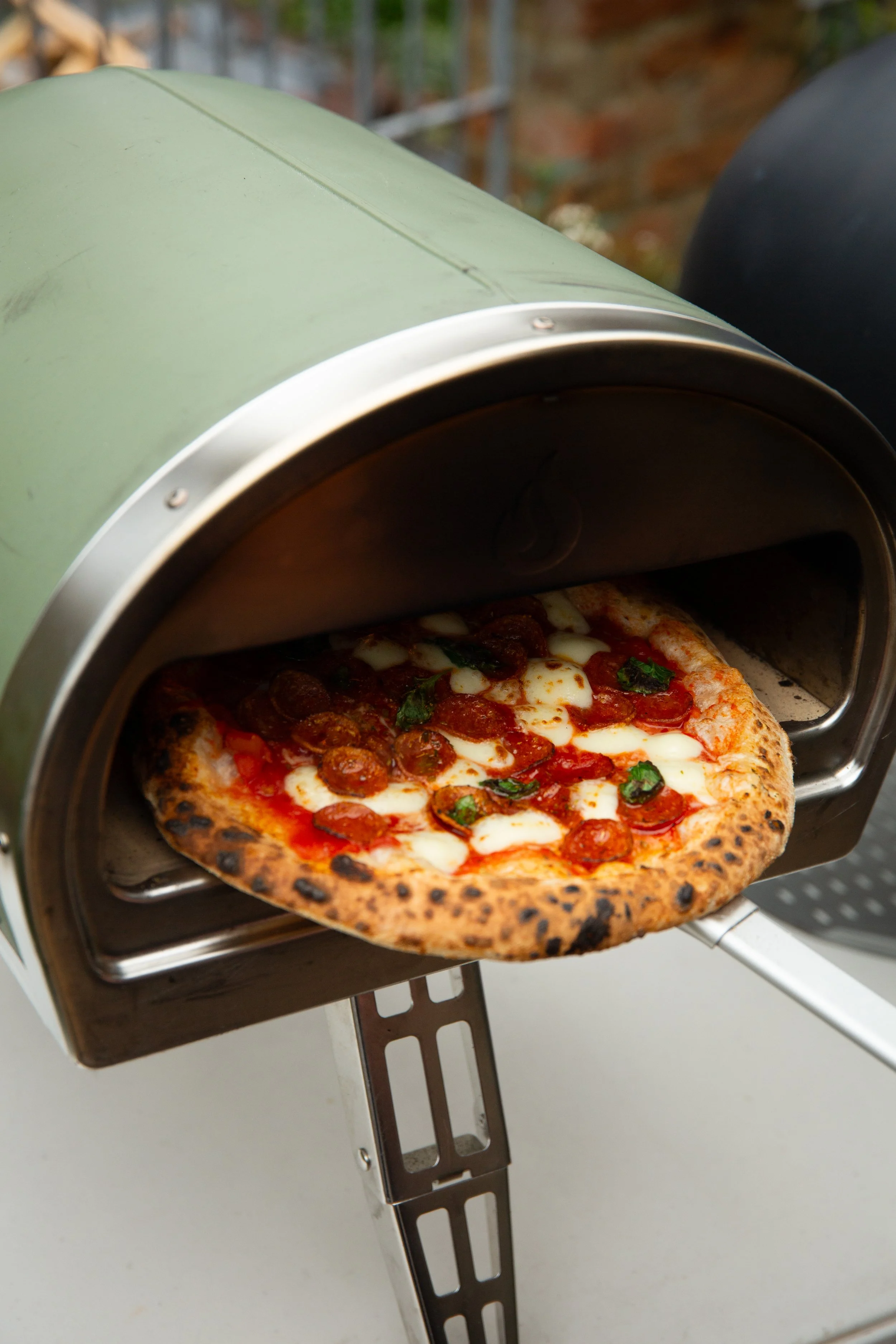 Pizza being cooked in a small, outdoor pizza oven.