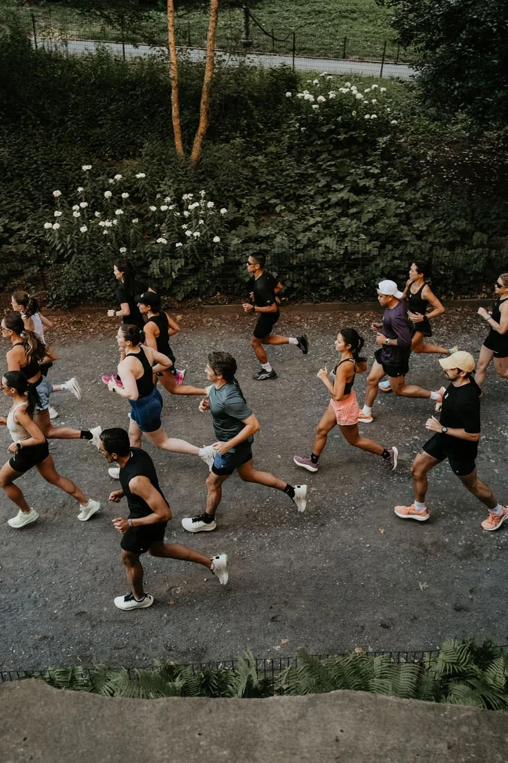 Groupe de personnes courant lors d'une session de running en extérieur sur un chemin asphalté entouré de verdure et de fleurs