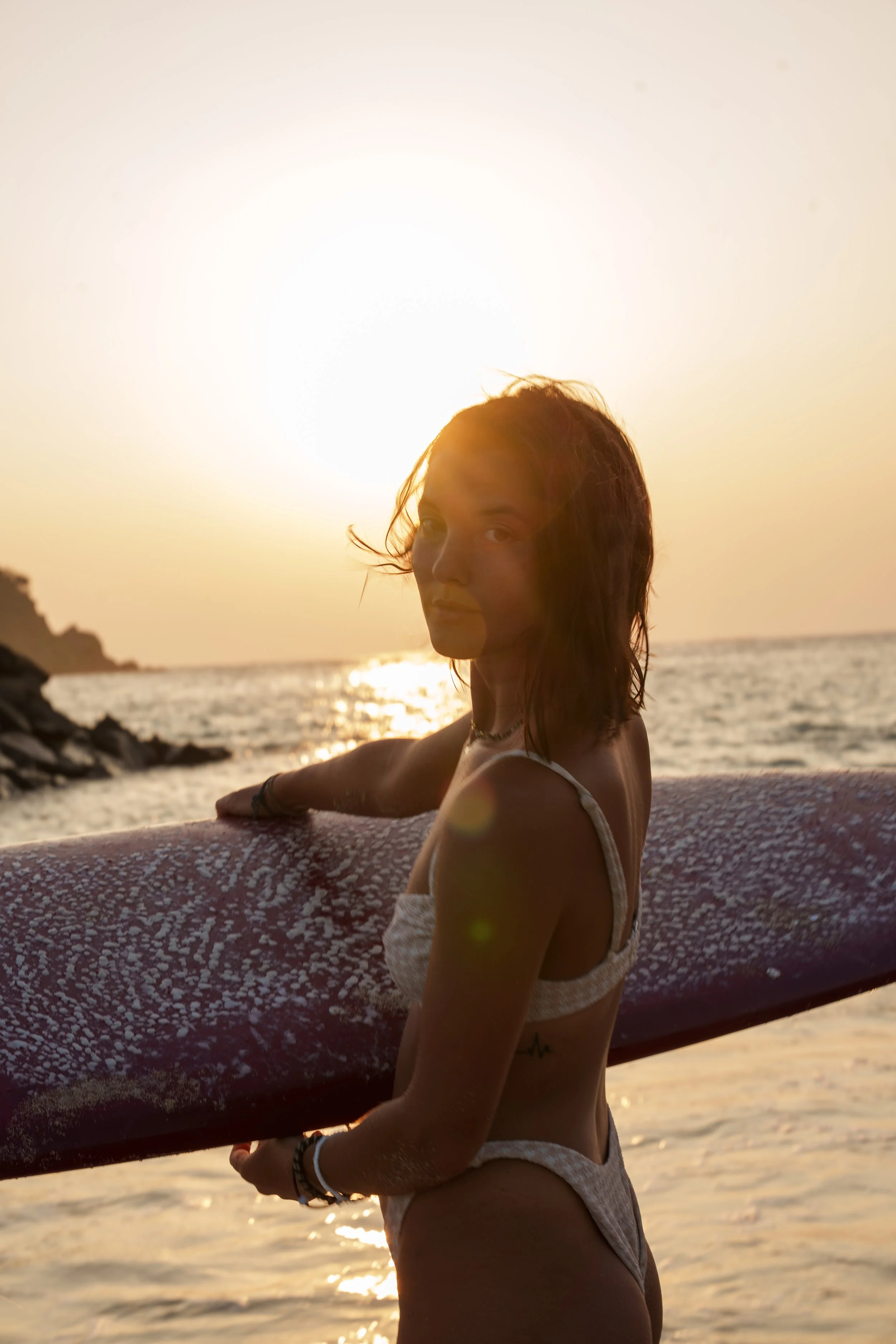 Jeune femme en maillot de bain tenant une planche de surf sur la plage au coucher du soleil.