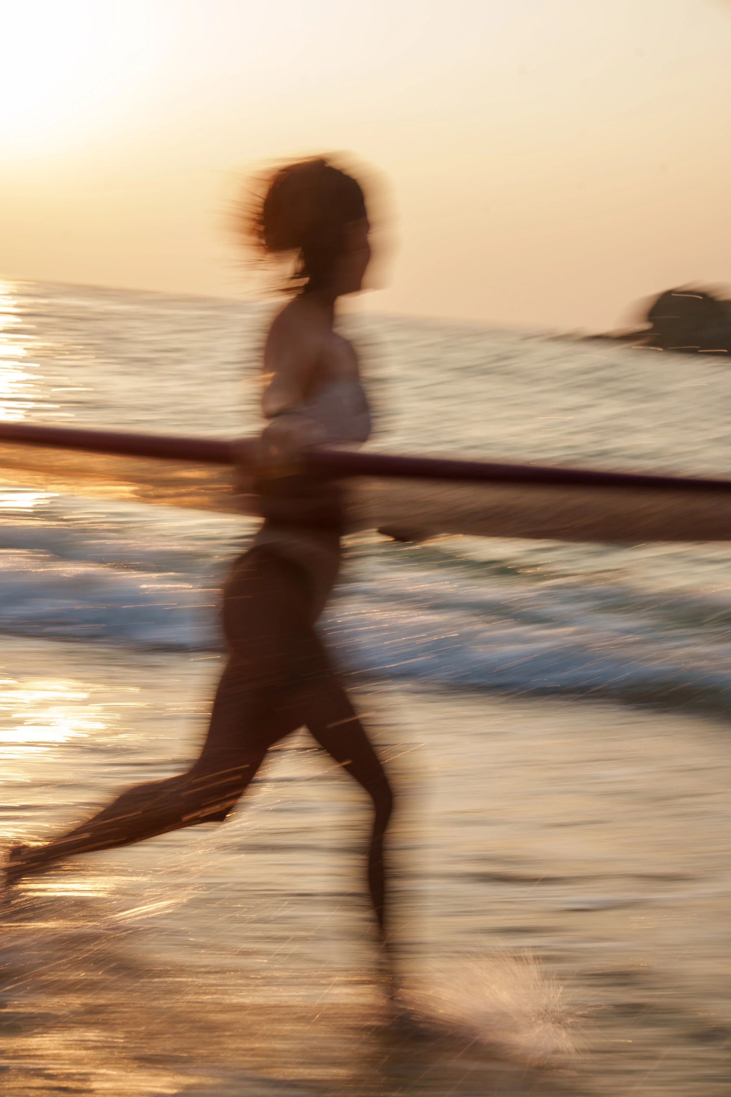 Silhouette floue d'une femme courant sur la plage avec un plan d'eau au coucher du soleil.