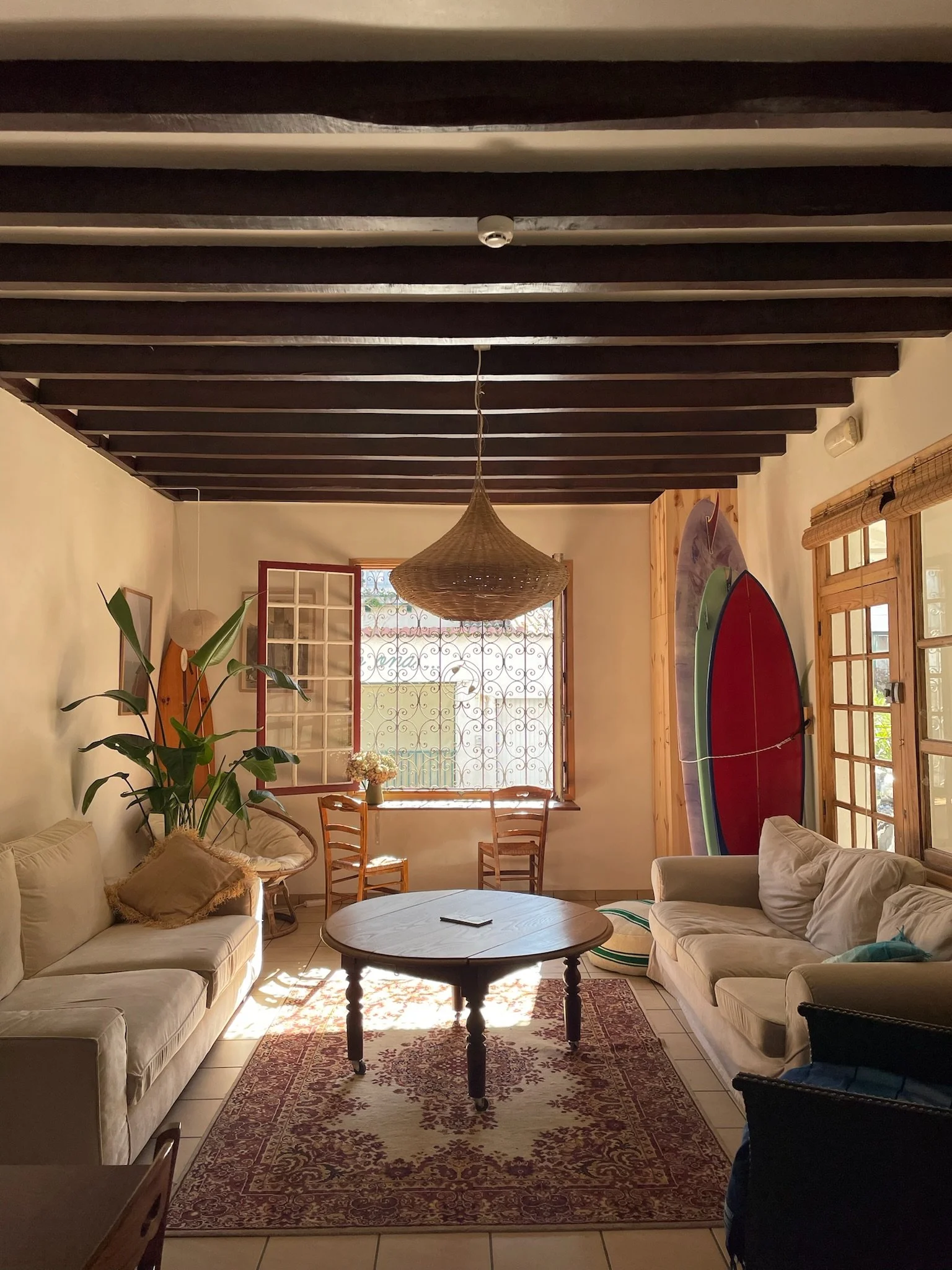 Salon avec deux canapés, une tapis, une table ronde, un rayon de soleil, deux paires de paddle sur le mur, plantes, fleurs, fenêtres et éclairage