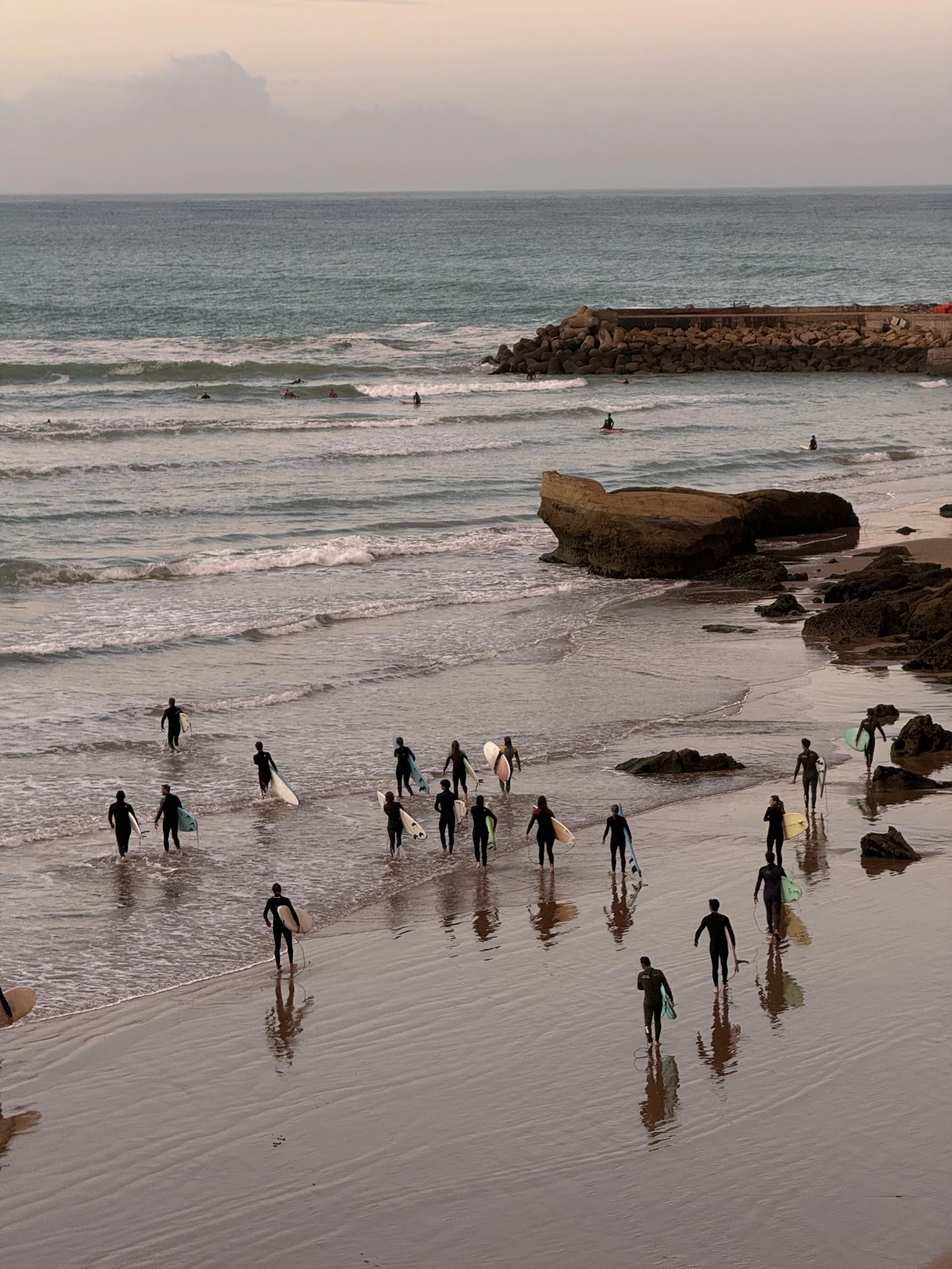 Groupe de surfeurs marchant vers la mer avec des planches de surf sur la plage au coucher du soleil.