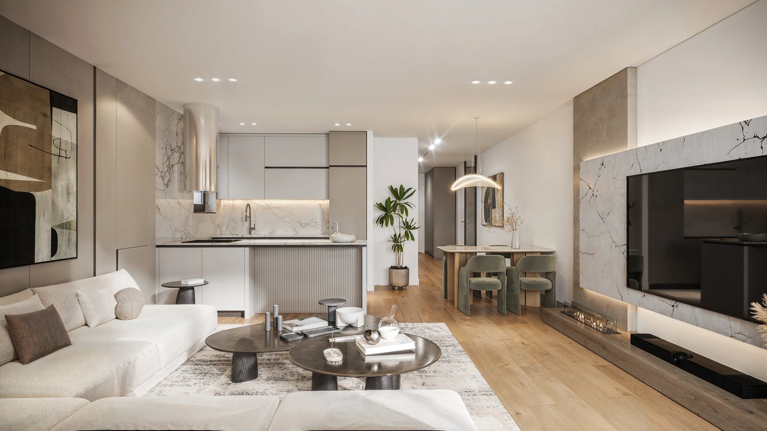 Modern living room with white sofa, wooden coffee tables, artwork on the wall, flat-screen TV on a marble accent wall, and an open kitchen with marble backsplash and a small dining area with green chairs.