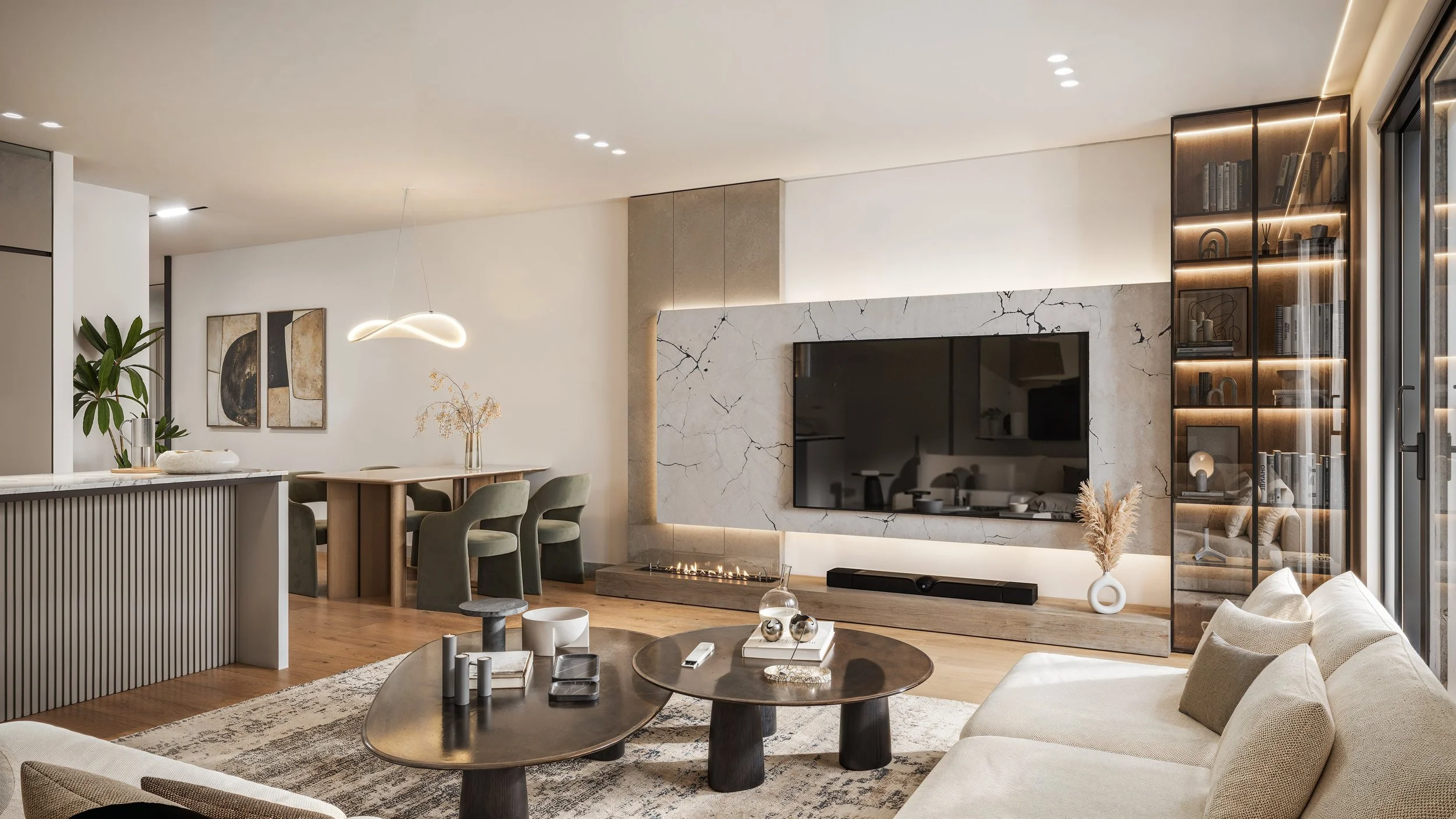 Modern living room with a beige sofa, two round coffee tables, fireplace, TV, glass-front bookshelf, and dining area with a wooden table and green chairs.
