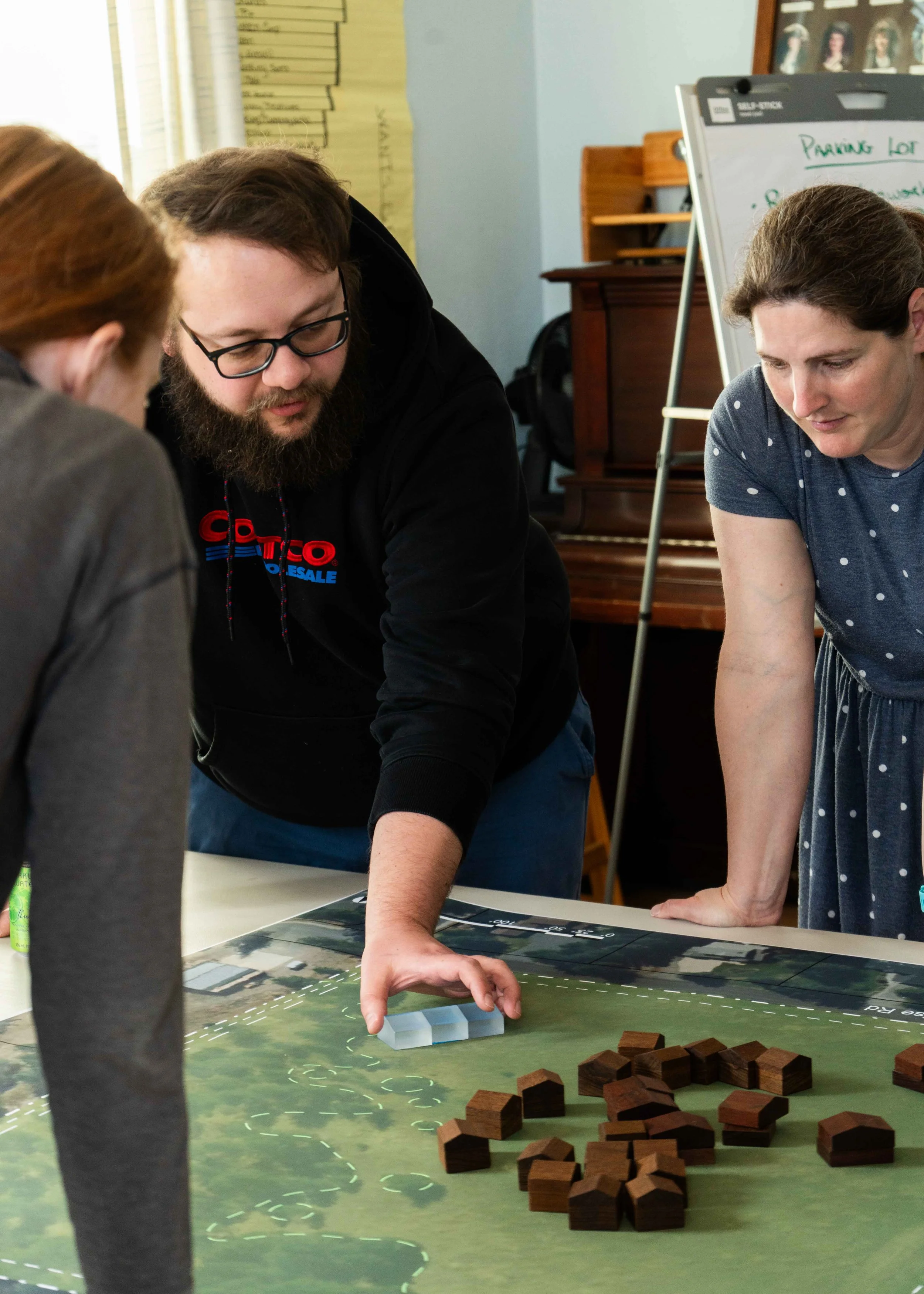 People gathered around a table with a map and game pieces, discussing or planning something.