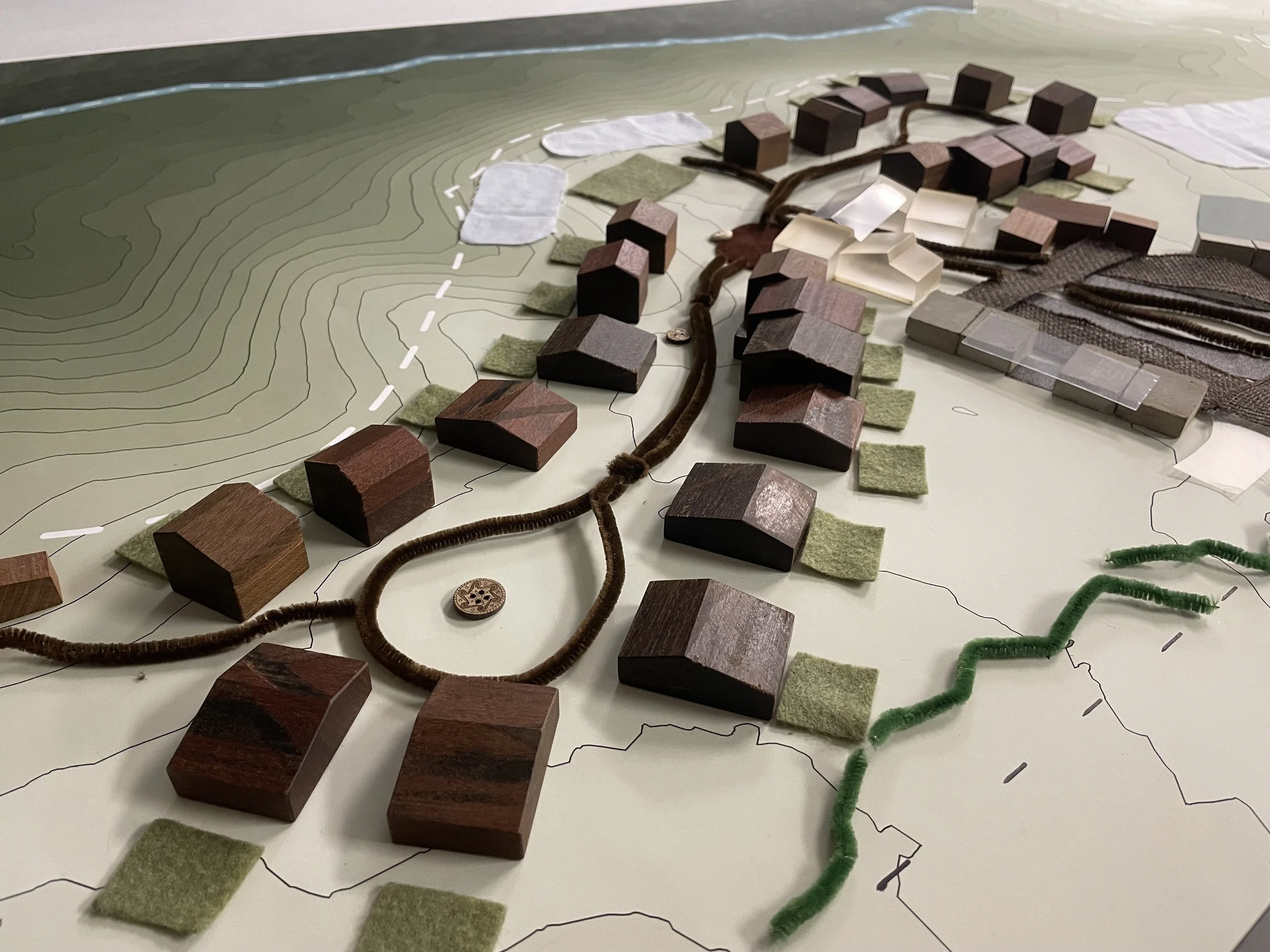 A detailed architectural model showcasing a community with several small houses, roads, pathways, and landscaping elements on top of a topographical map with contour lines.