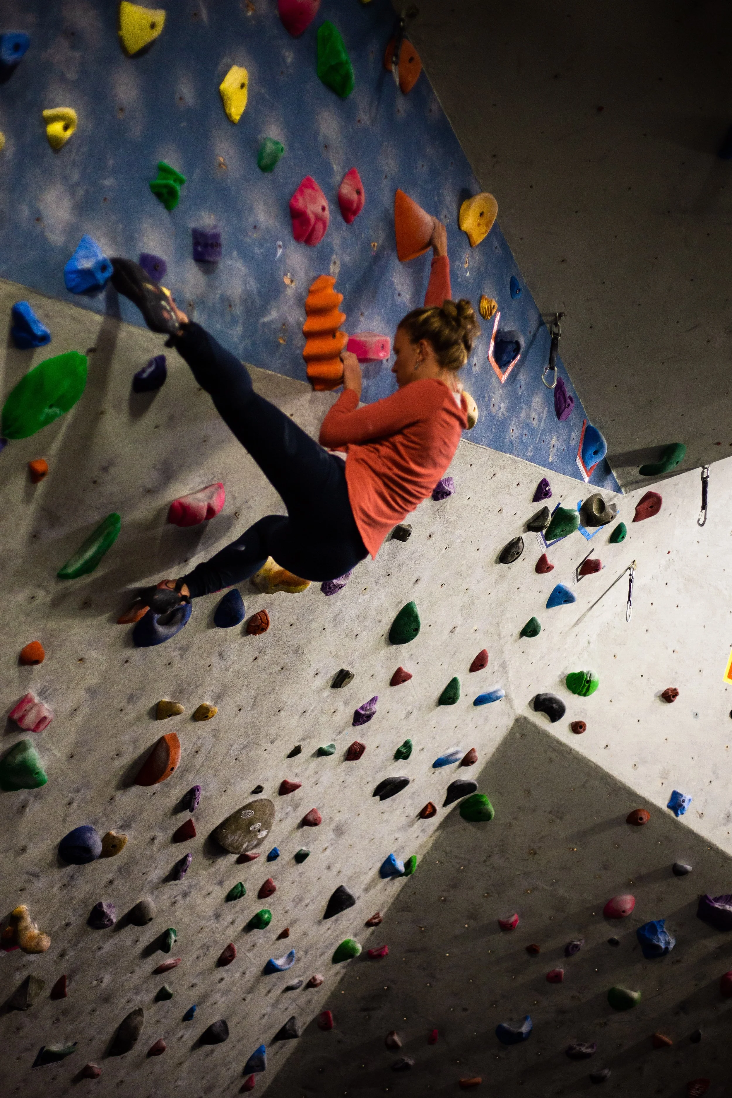 A woman climbing an indoor rock wall with colorful holds.