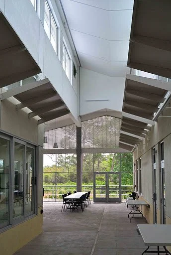 Enclosed outdoor patio with a table and chairs, surrounded by large glass windows and view of green trees outside.