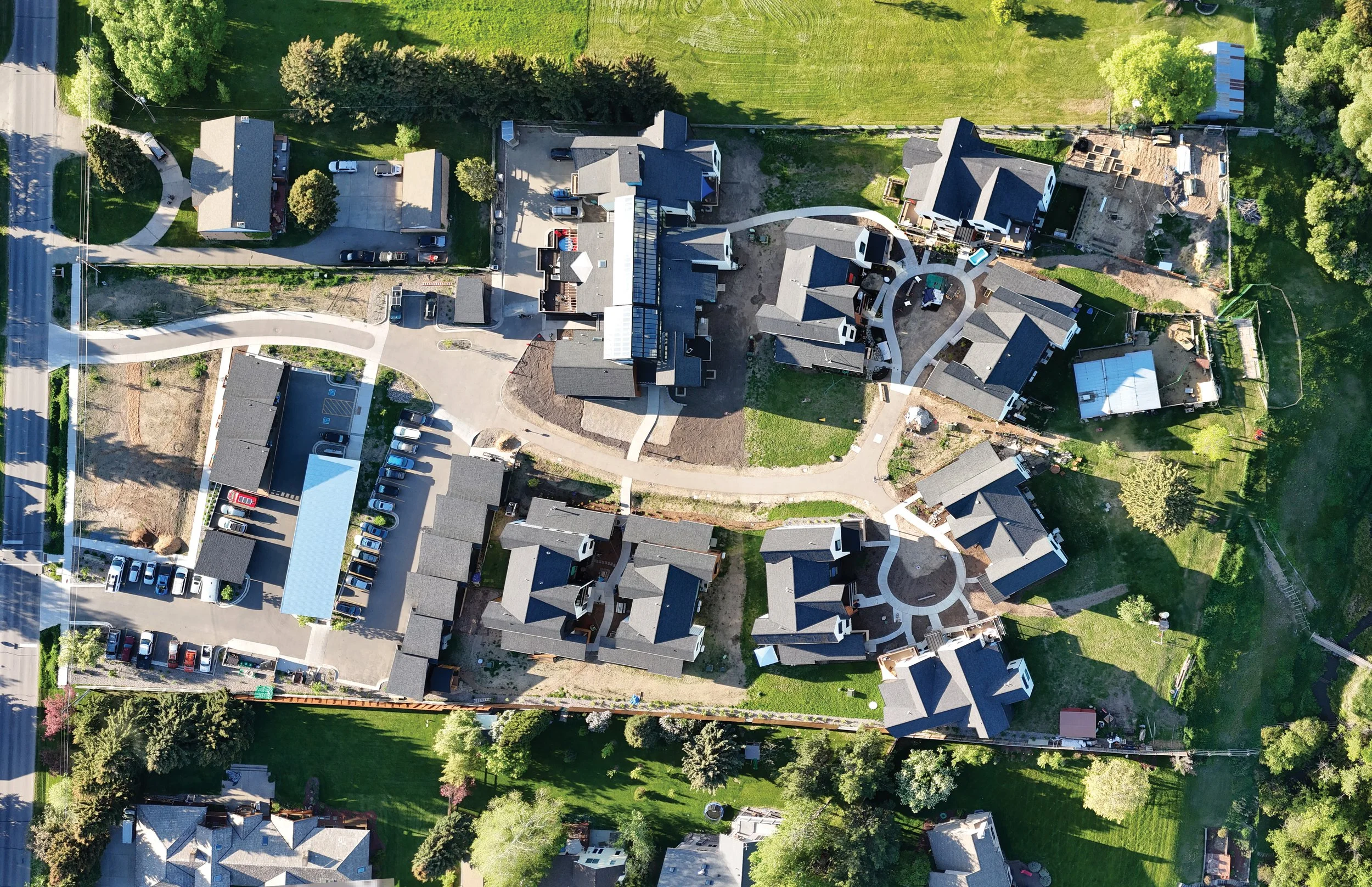 Aerial view of a residential neighborhood with houses, green lawns, trees, and parked cars along the streets and in driveways.