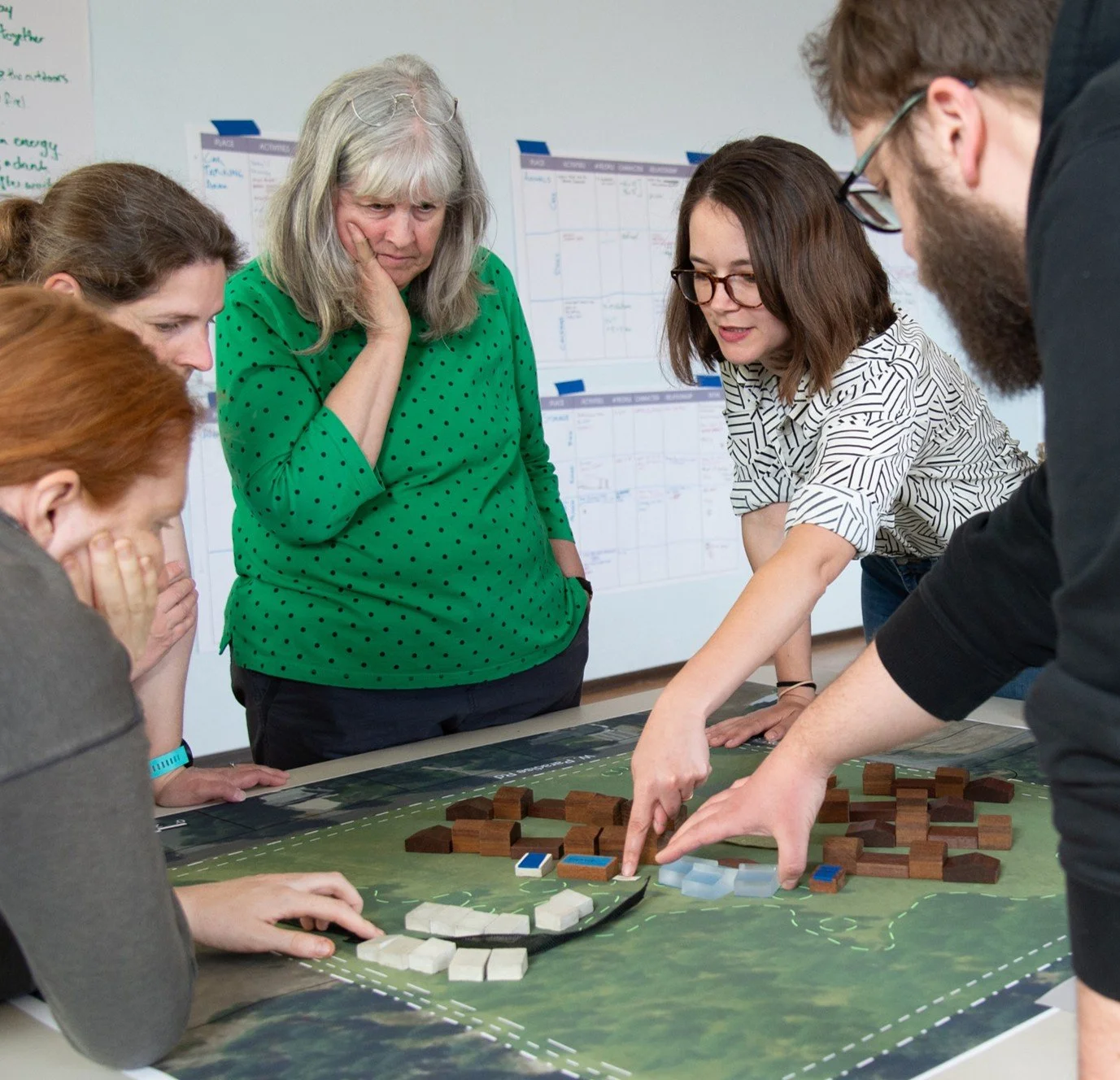 Group of people playing an educational board game with game pieces on a table.