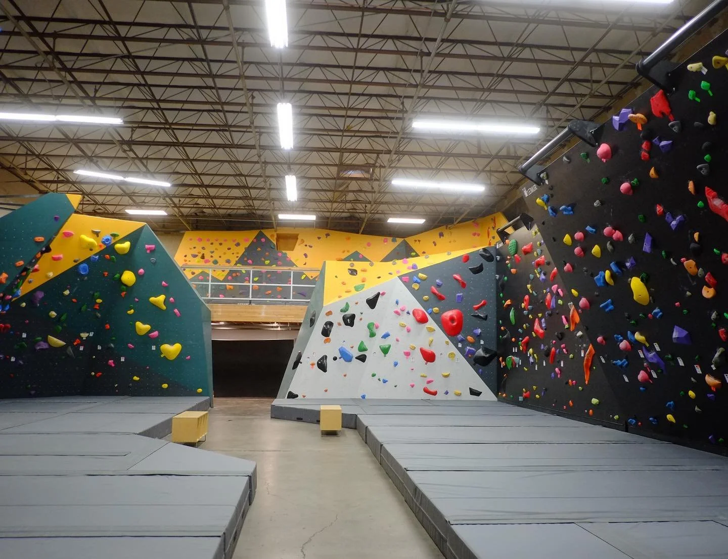 Indoor bouldering gym with colorful climbing walls, padded flooring, and climbing holds in various shapes and colors.