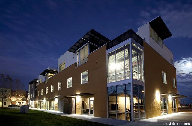 Modern multi-story building with large glass windows illuminated at night.