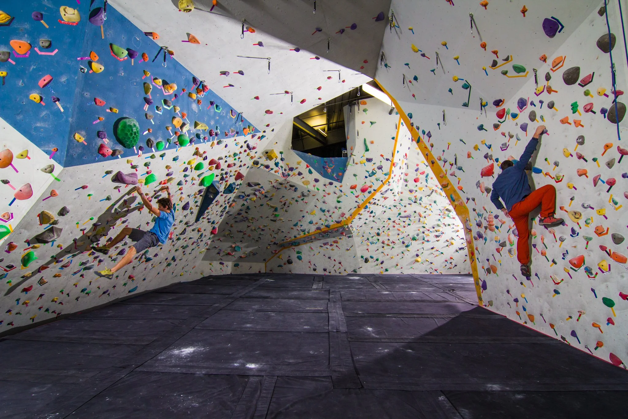 Indoor rock climbing gym with colorful climbing holds on walls and two climbers ascending.