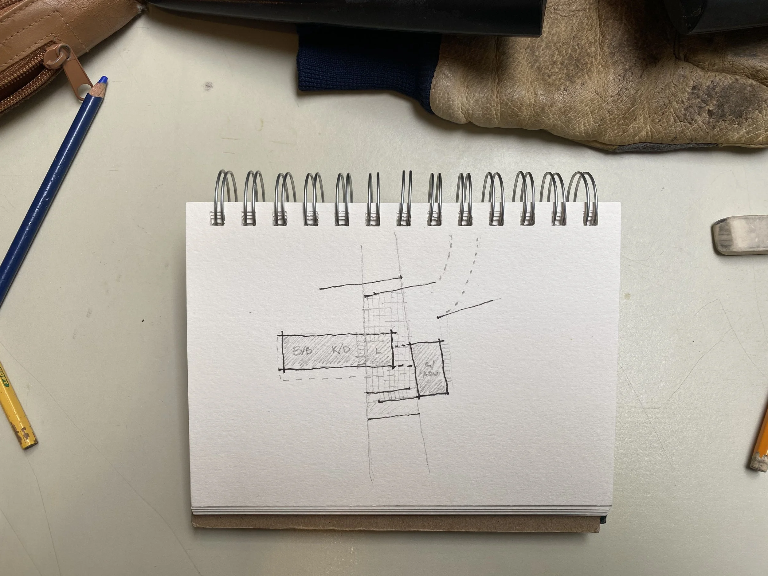Overhead view of a desk with a spiral notebook featuring a hand-drawn diagram, colored pencils, and various office items.