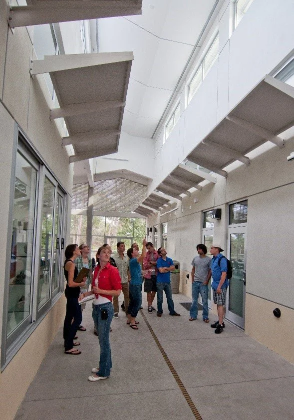 Group of people waiting in line at a modern indoor space with large windows and architectural overhangs.